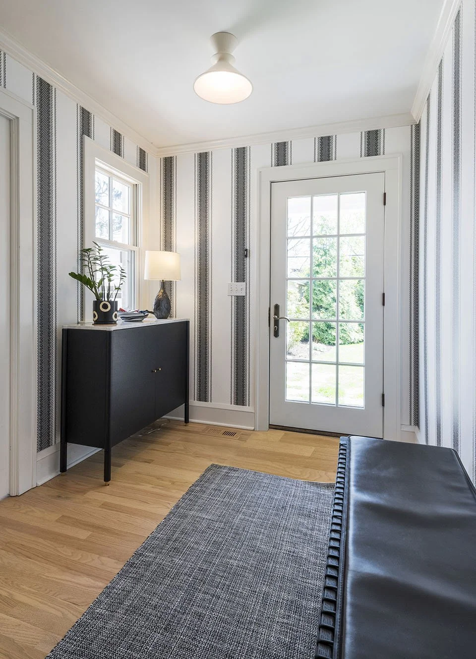 Bright entryway with a navy blue area rug, striped wallpaper, white trim, and natural light from a glass-paneled door | Ducy Design