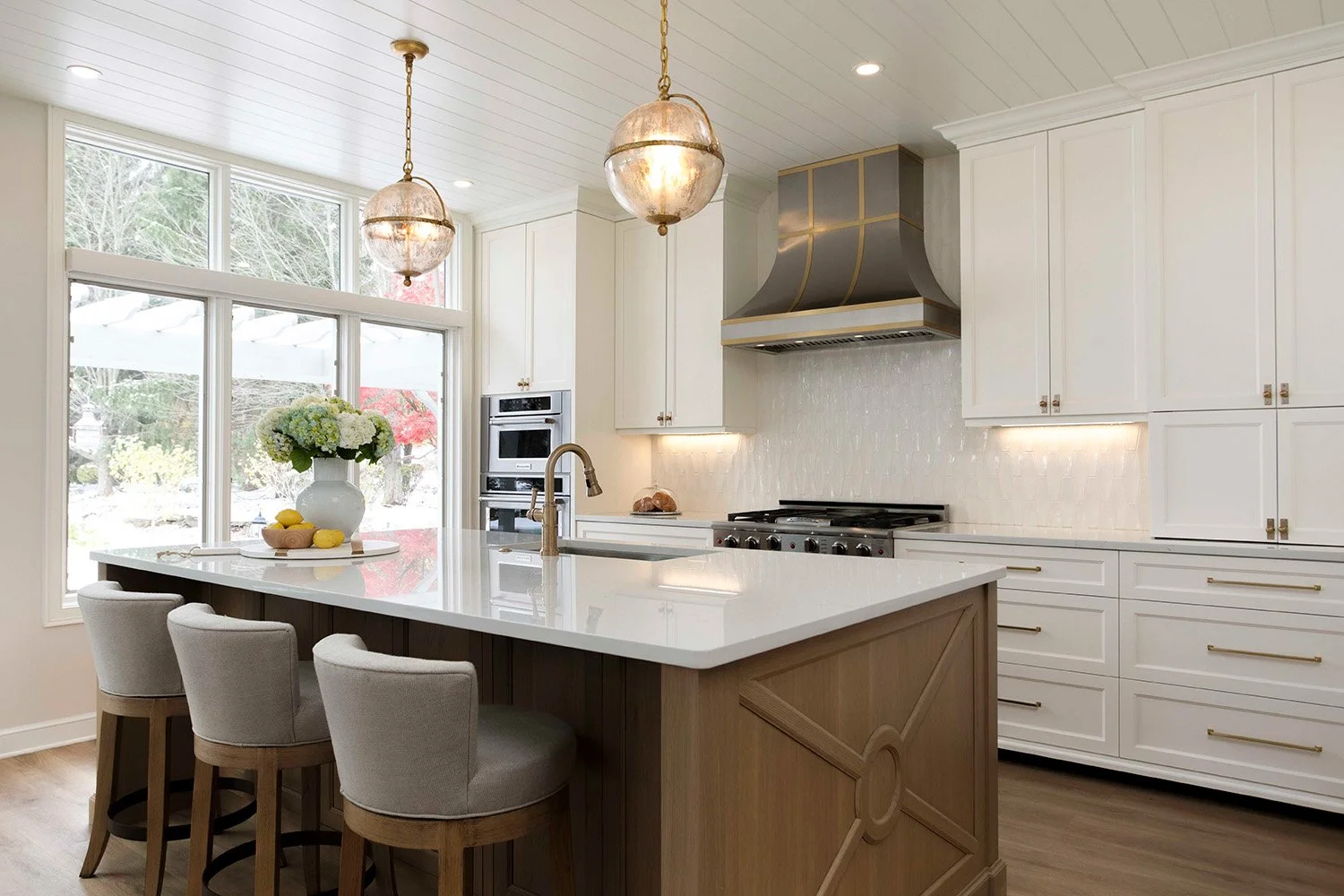 Kitchen with a wood and quartz island, white perimeter cabinetry, mixed metal pendant lighting, aged brass hardware, and a professional range wall | Ducy Design