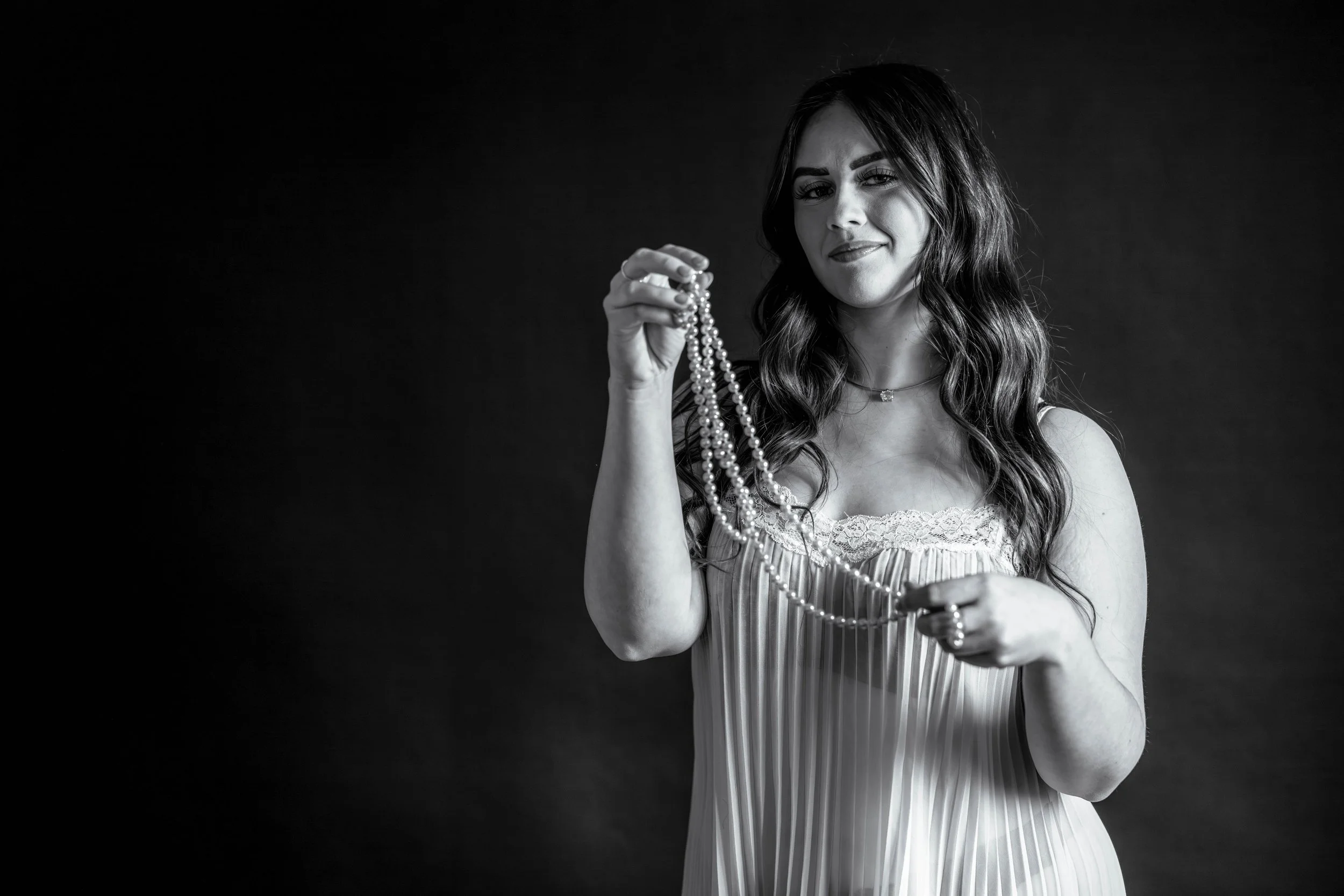 You don't have to wear the pearls to have them help you look uniquely you in  your bouidoir session. This woman in her sheer pleated short gown plays with a string of pearls in her hands in a way that suggests something evocative and sensual.