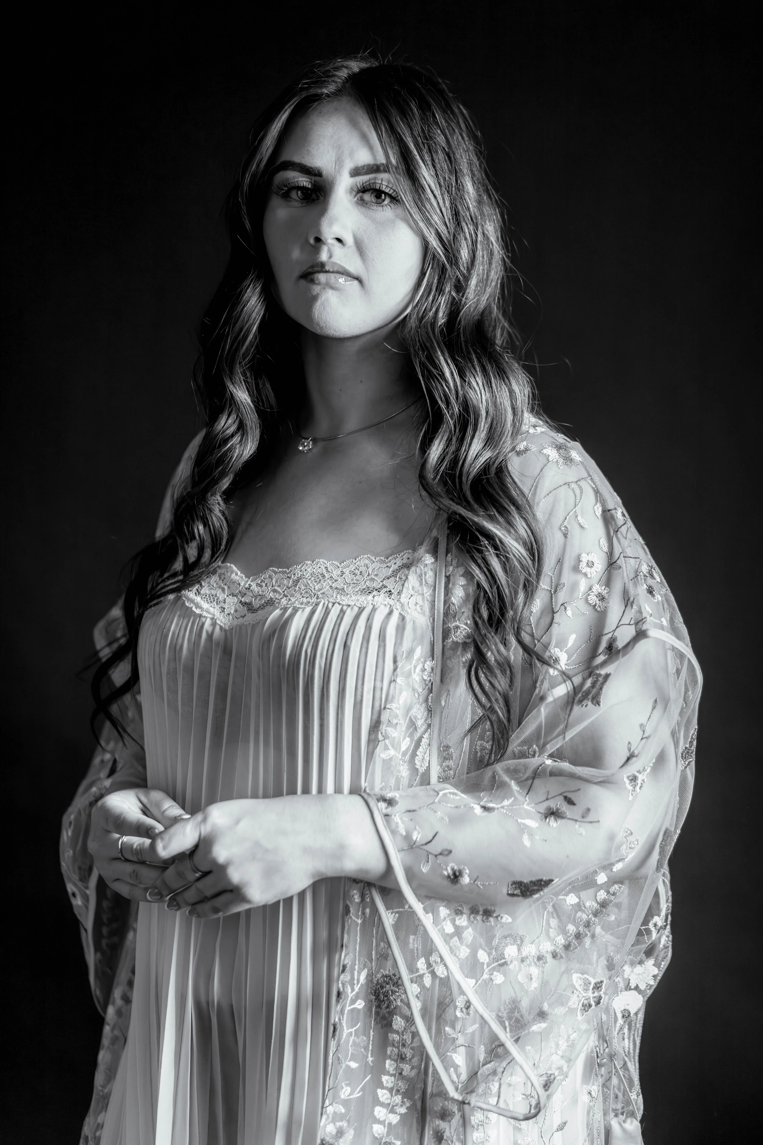 This image of a dark haired woman in a light pleated sheer gown with her dark lingerie showing, demonstrates the beauty of allowing your boudoir session be unique to you.