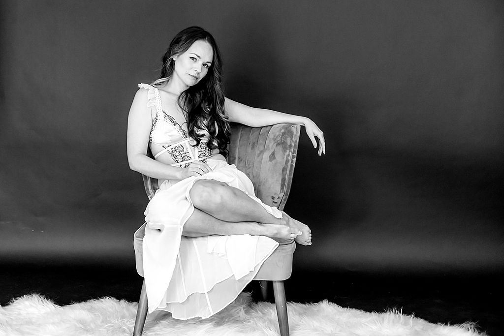 Woman wearing a white lingerie gown, curled up on a vintage chair
