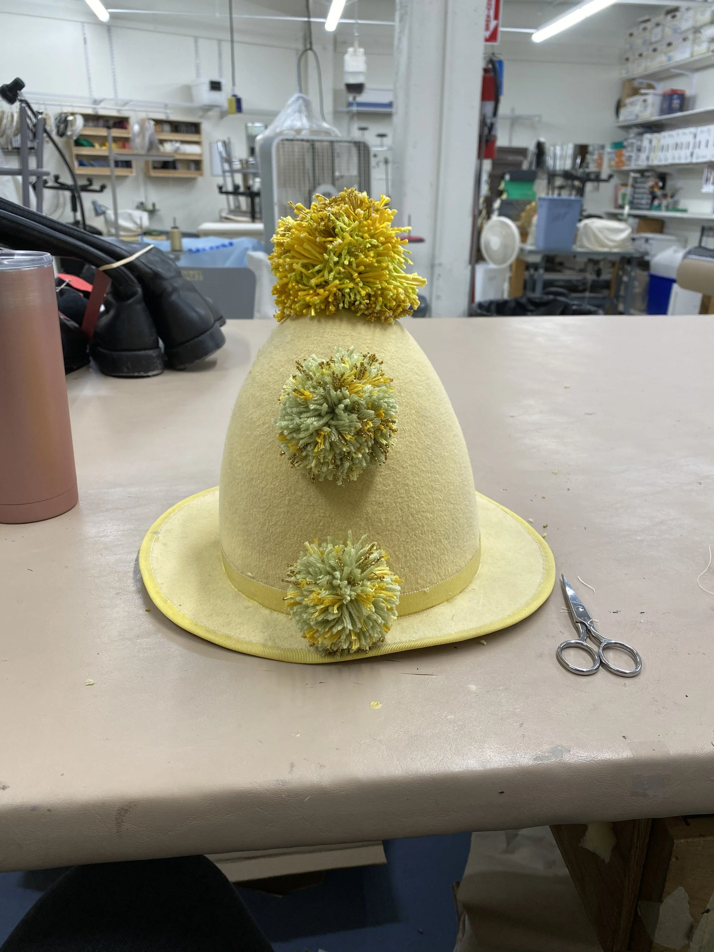Created bottom and middle pompoms to match top pompom found in stock. Stitched onto hat. Santa Fe Opera Apprentice Scenes 2021. Designer: Yamilex Holguin.