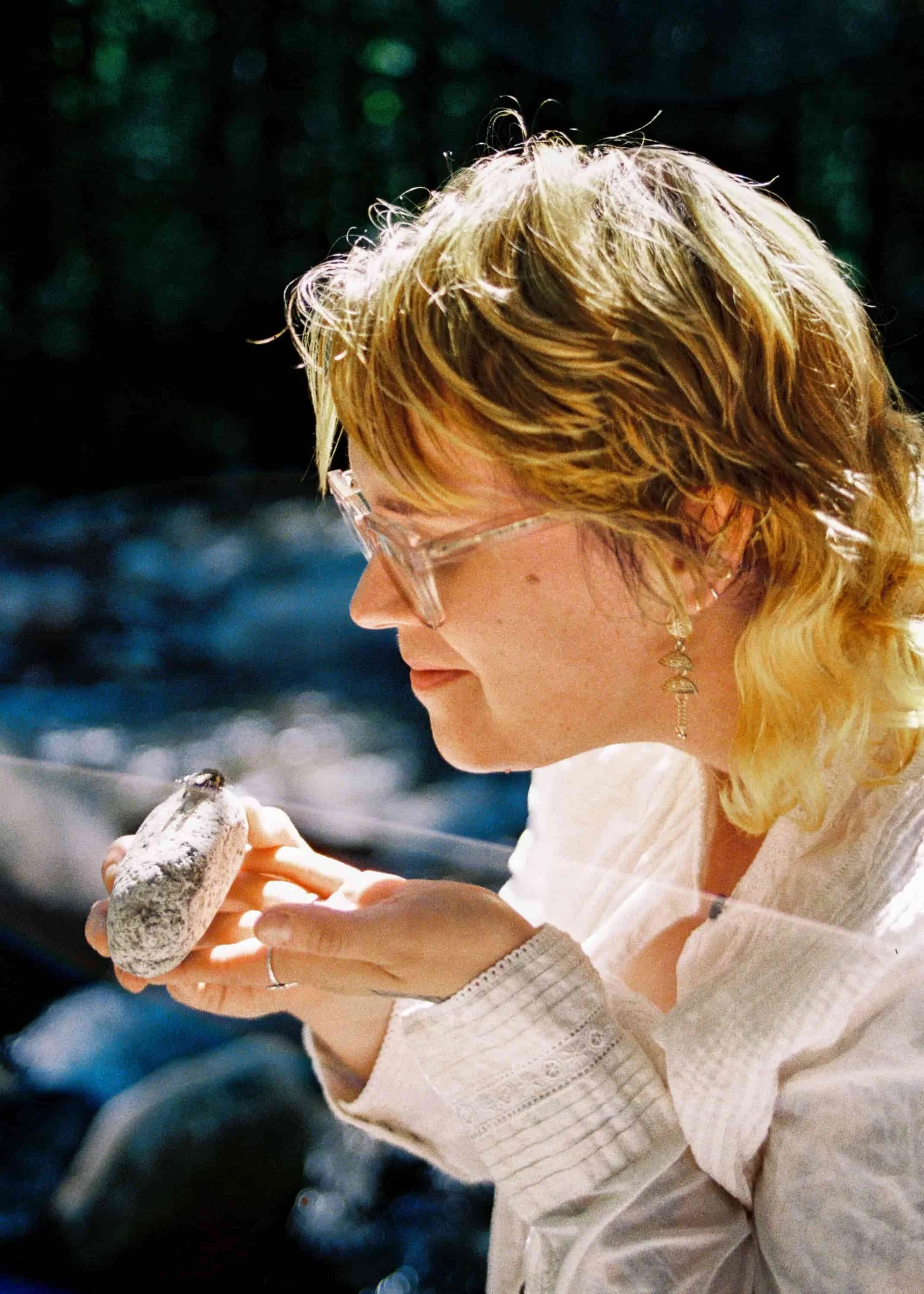 Michelle has yellow hair and is looking at a bee with compassion at the river in North Vancouver, she is a wonderful doula