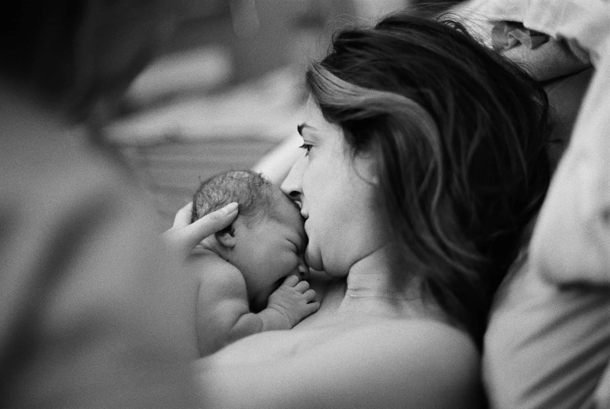 Postpartum mom with newborn giving them a kiss
