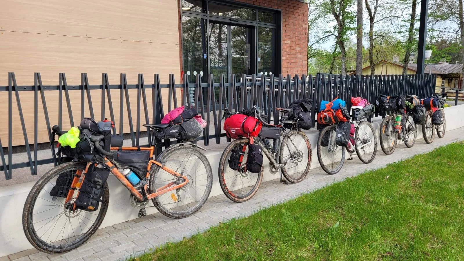 Useita bikepacking-pyöriä parkissa rakennuksen vieressä, varusteet kiinnitetty runkoon ja laukkuun
