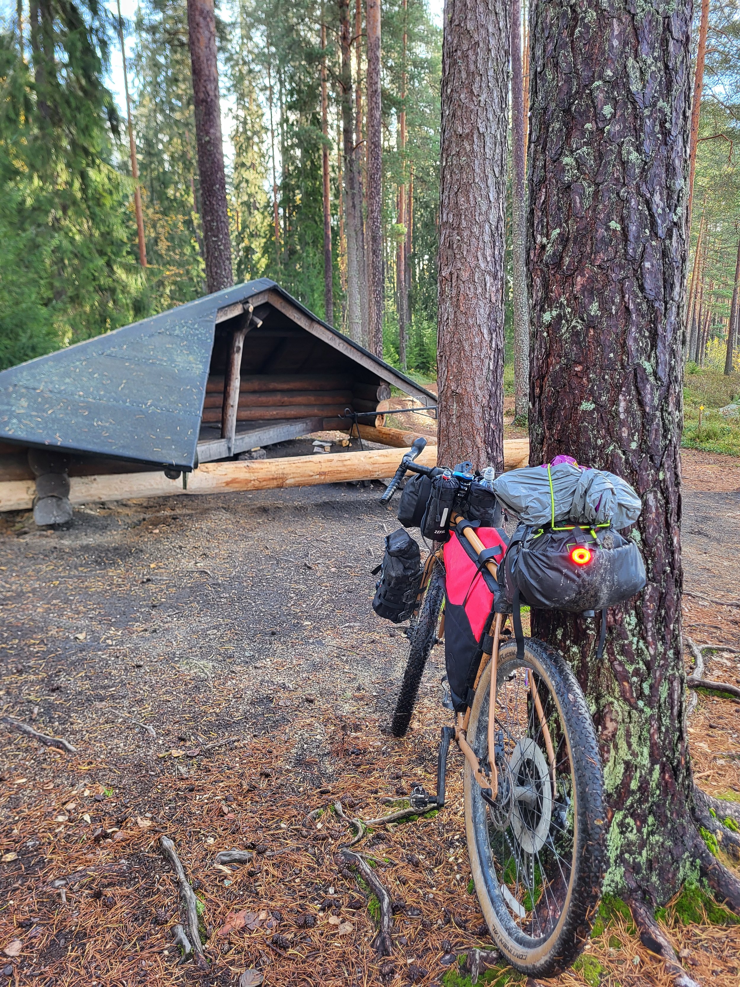 Bikepacking-pyörä nojaamassa puuhun laavun vieressä metsässä, retkivarusteet pakattuna pyörään