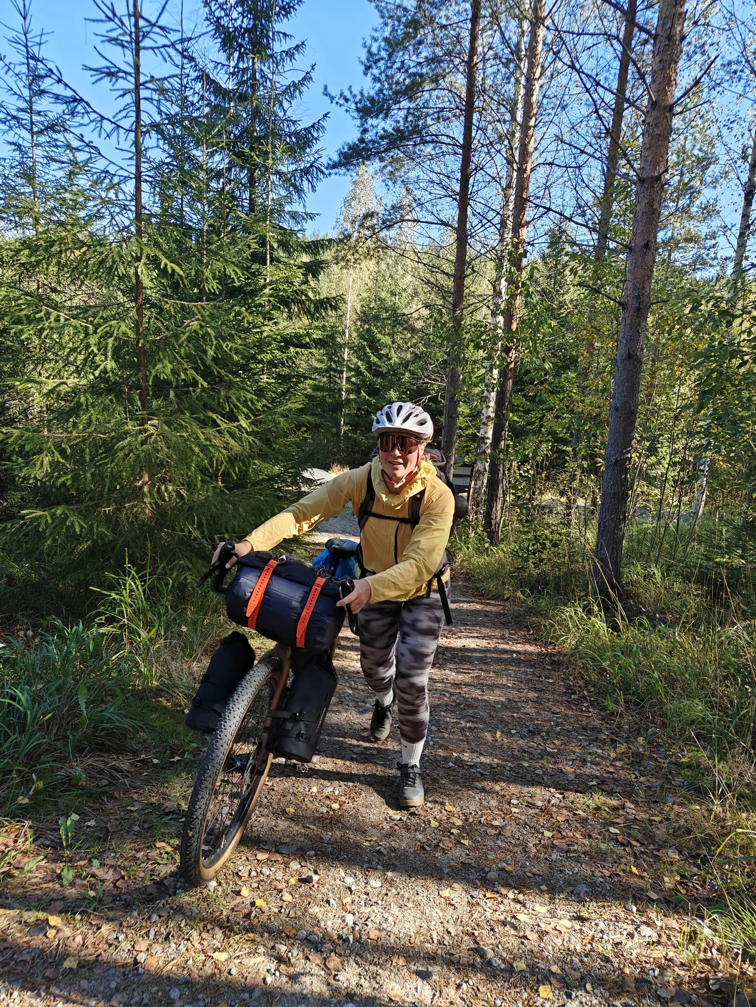 Bikepacking-pyöräilijä taluttamassa varusteltua pyörää metsäpolulla, retkipyöräily luonnossa