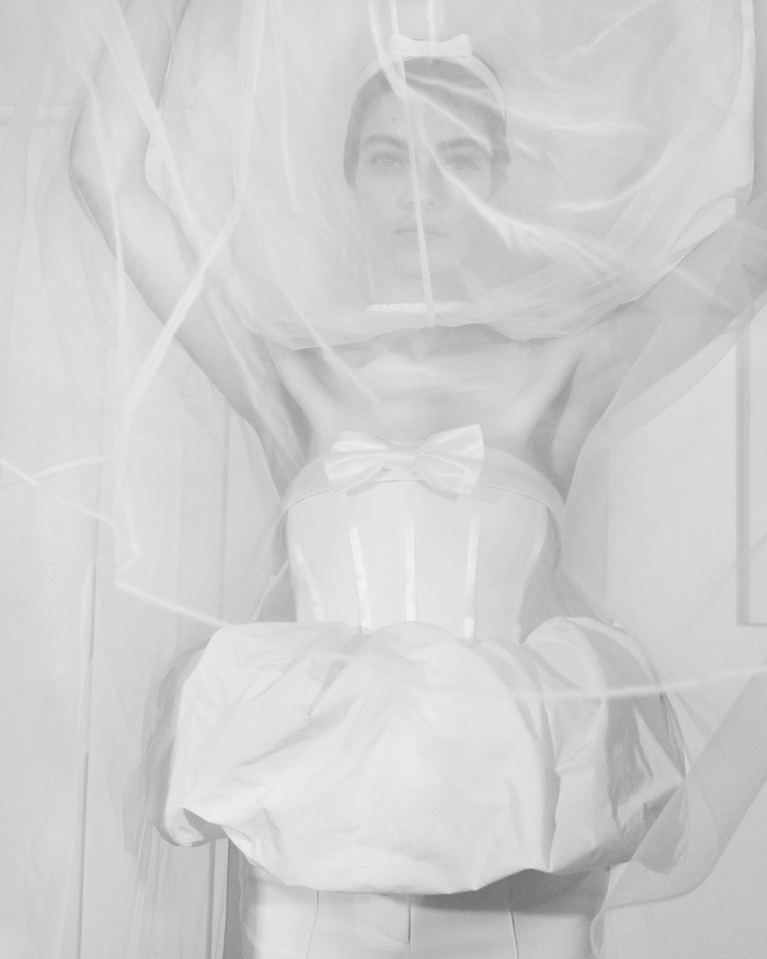 A woman dressed in white with a bow in the middle of her dress, visible through a sheer, billowing fabric.