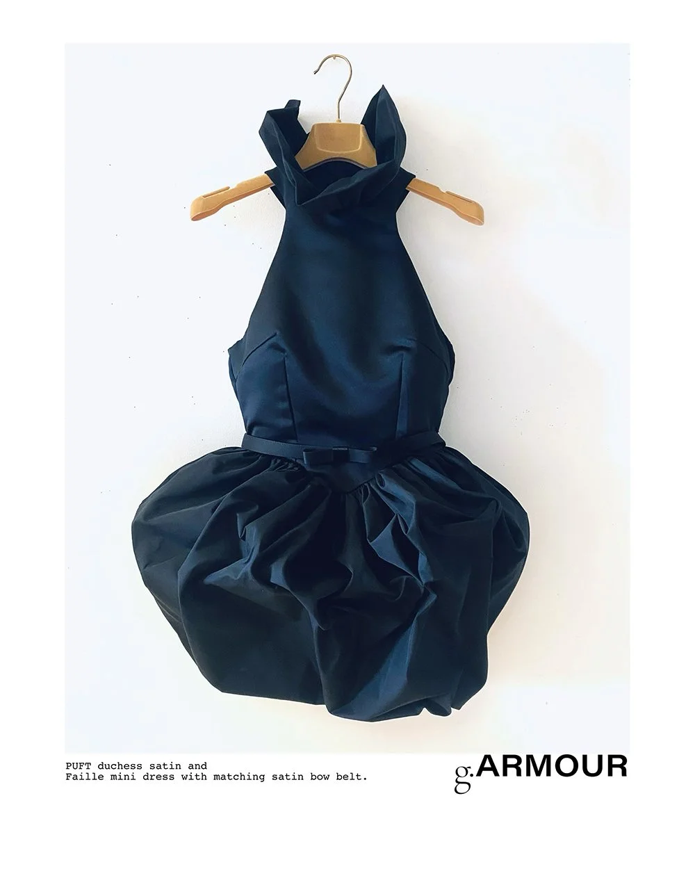 A black mini dress with a satin bow belt hanging on a wooden hanger against a white background.