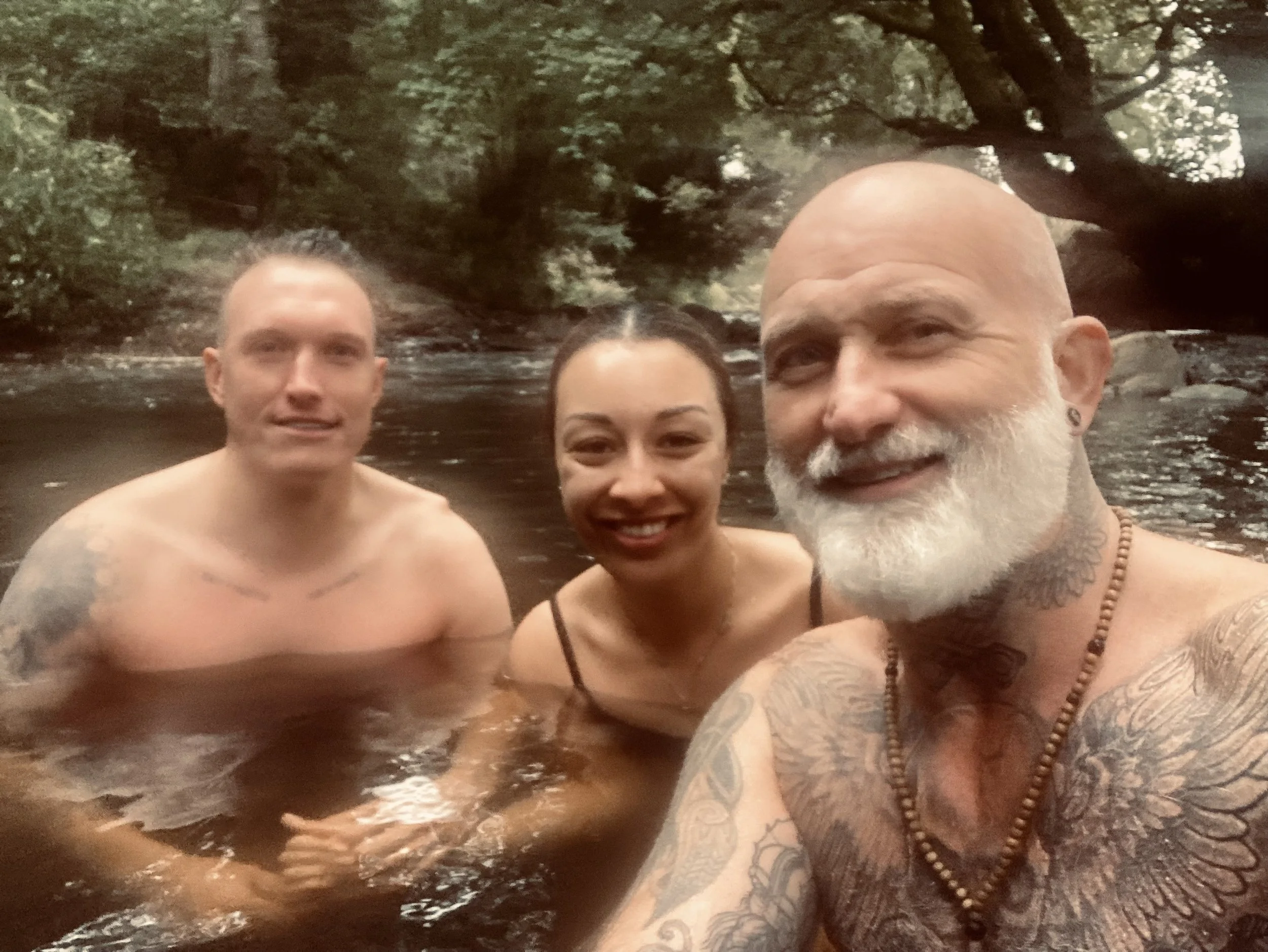 Three people taking a selfie in a river surrounded by trees.