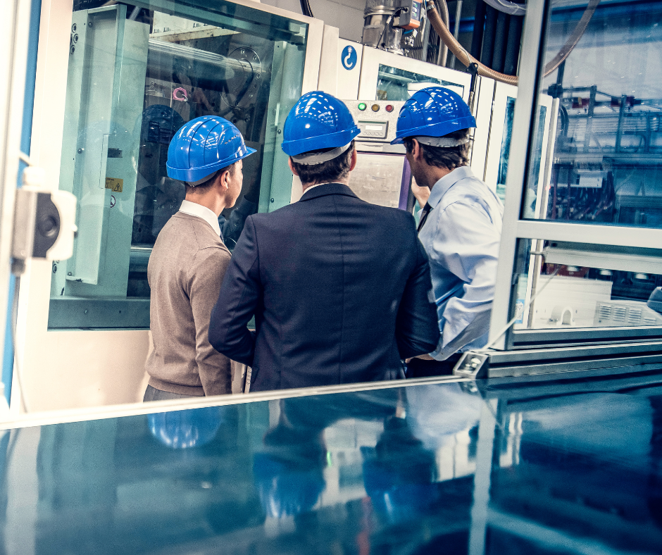 Three professionals, wearing blue safety helmets, are inspecting machinery in an industrial setting.