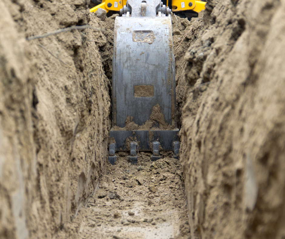 Close-up of an excavator bucket digging a trench in the dirt.