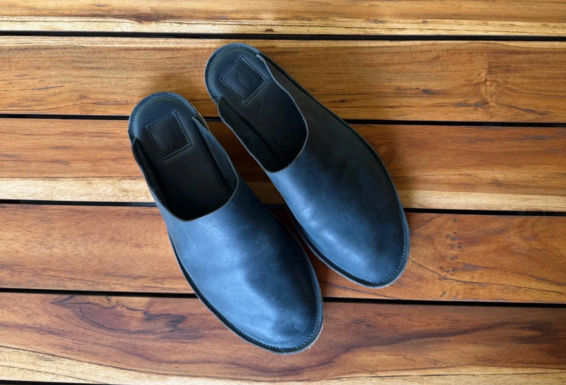 A pair of black leather slip-on shoes placed on a wooden floor with horizontal planks.