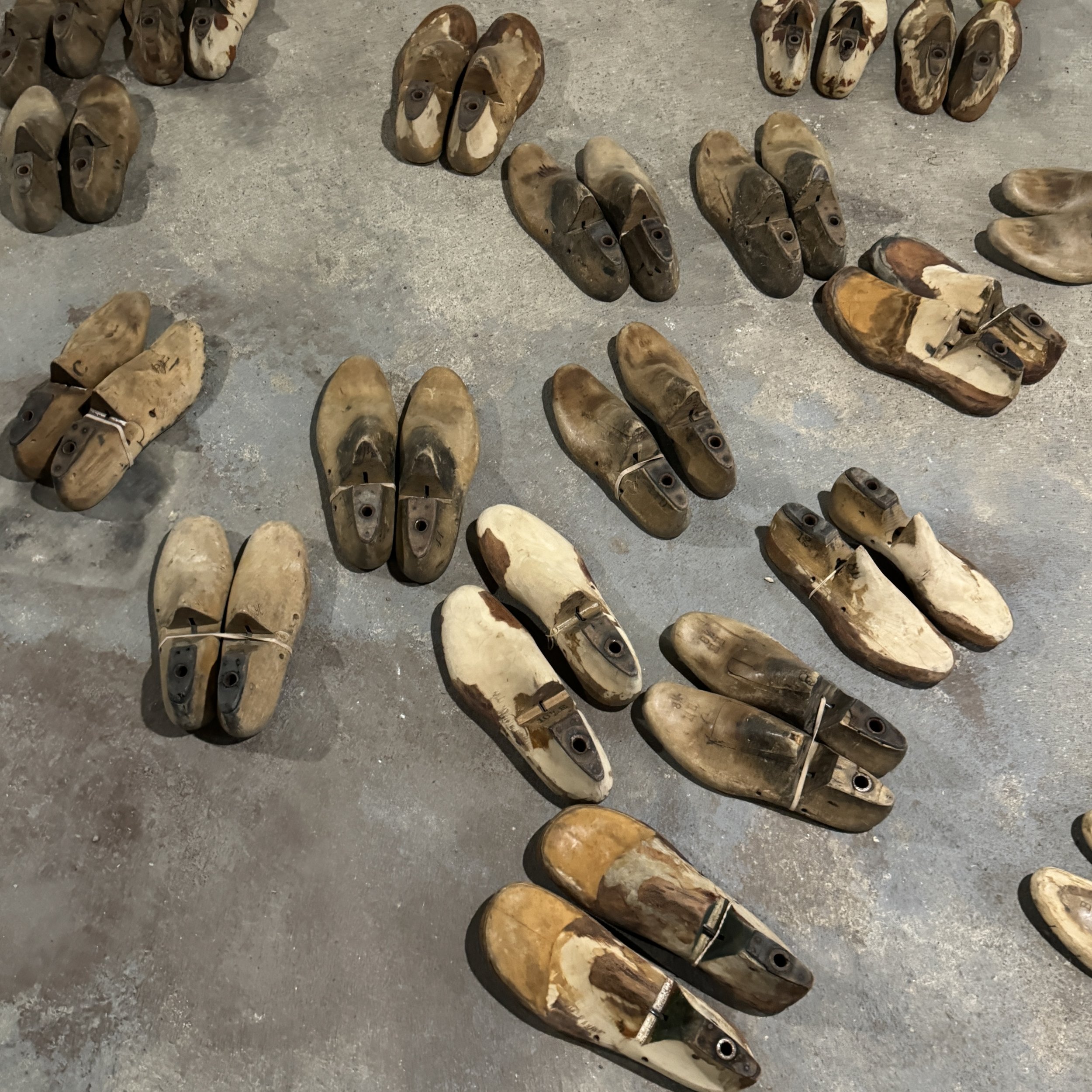 Multiple worn wooden shoe lasts arranged on a concrete floor, used for shaping and repairing shoes.