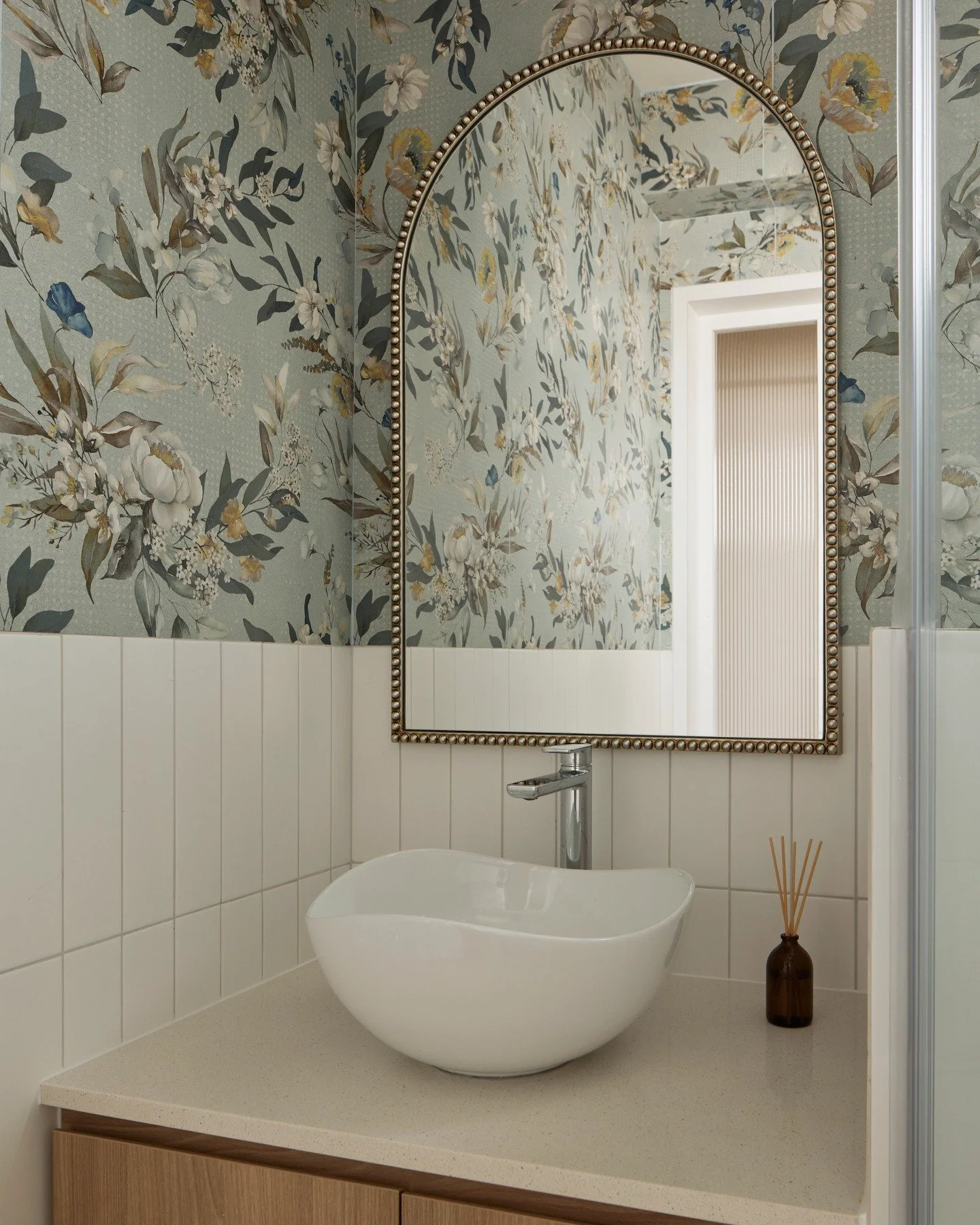 The floral tile is undoubtedly the star in this bathroom, but it shines only because everything else gels.

From the clam-like sink, to the beaded mirror and the chrome accessories, each plays a supporting (and no less important) role, to make this c