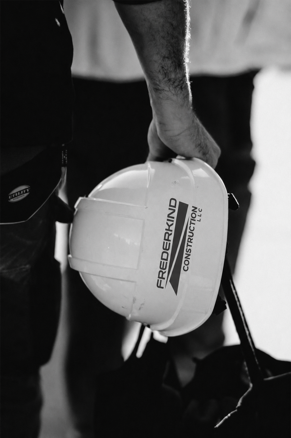 A construction worker holding a helmet with the label 'FREEDERKIND CONSTRUCTION LLC', taken in black and white.