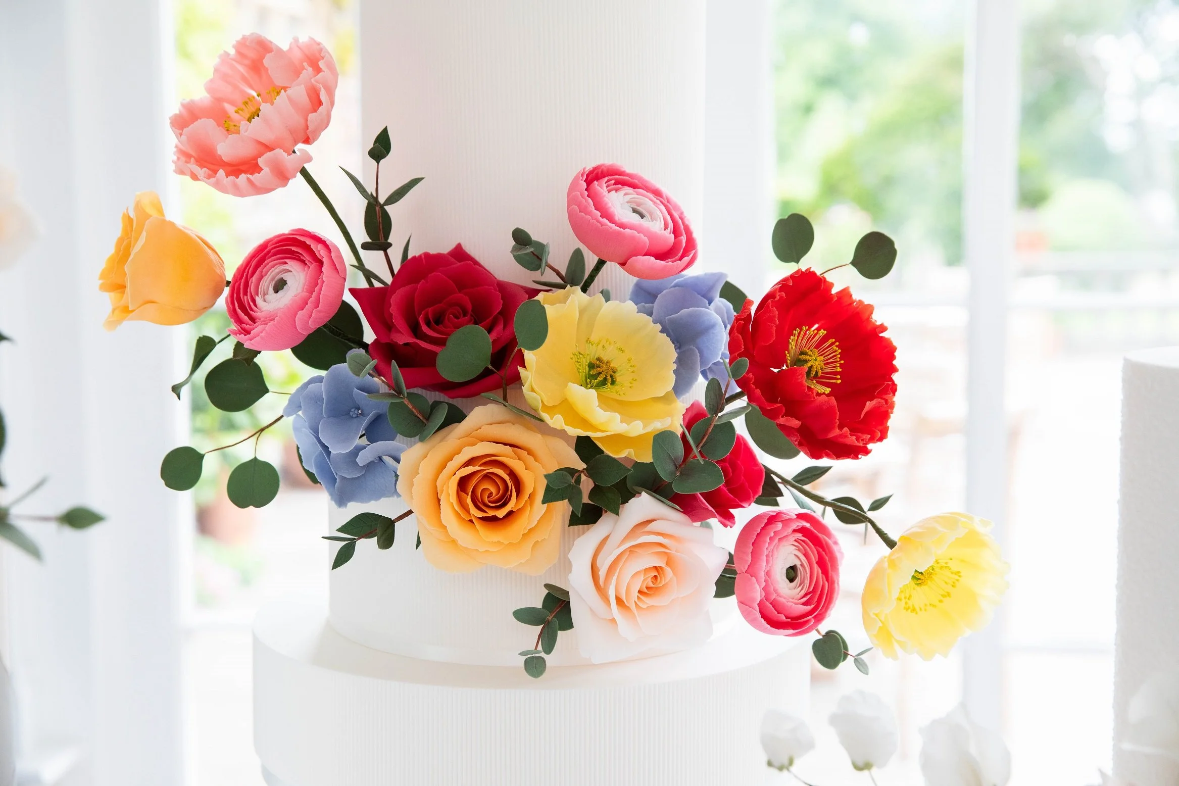 Image shows lots of different coloured flowers on the top of a wedding cake in the Orangery at North Yorkshire venue Goldsborough Hall