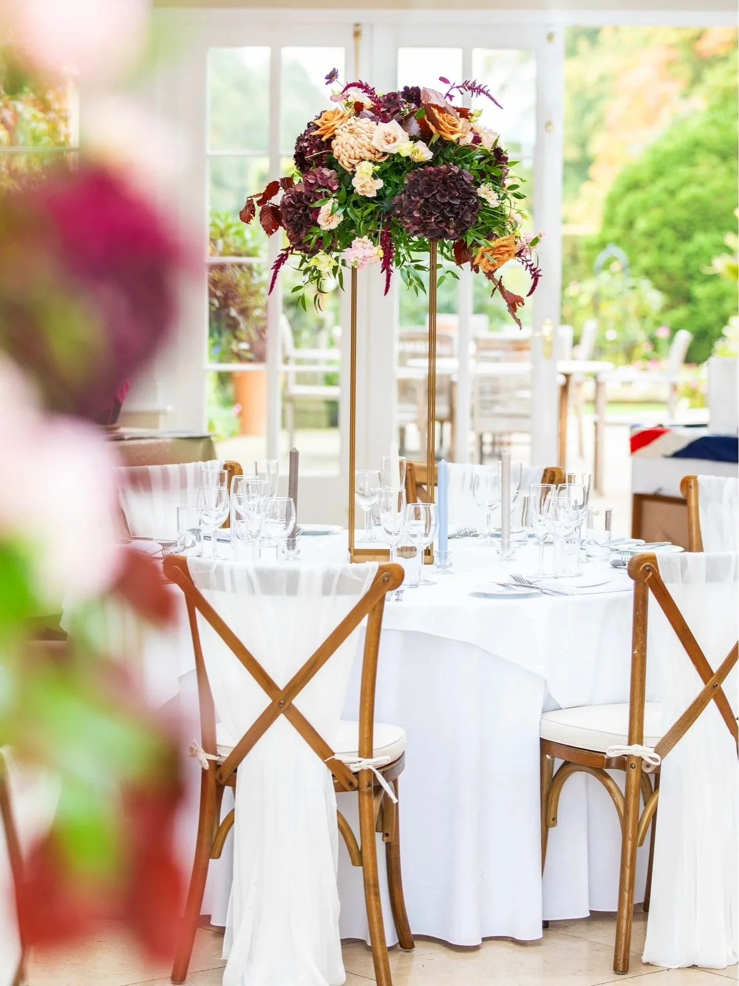 Image shows a wedding table with brown crossback chairs, white linen and a flower arrangement on the top in the Orangery at North Yorkshire wedding venue Goldsborough Hall