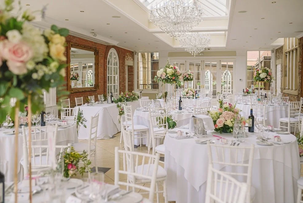 wedding breakfast with clothed tables, white chairs and flowers in the centre all set in an Orangery