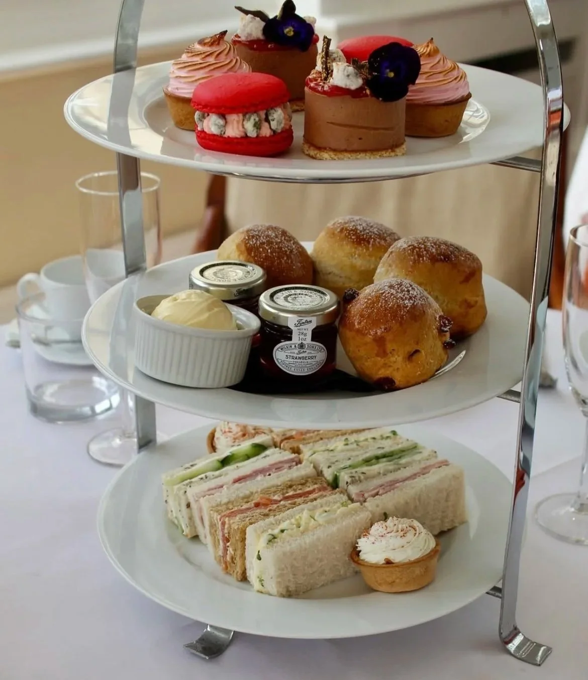 Three tiered afternoon tea stand with finger sandwiches, scones and cakes