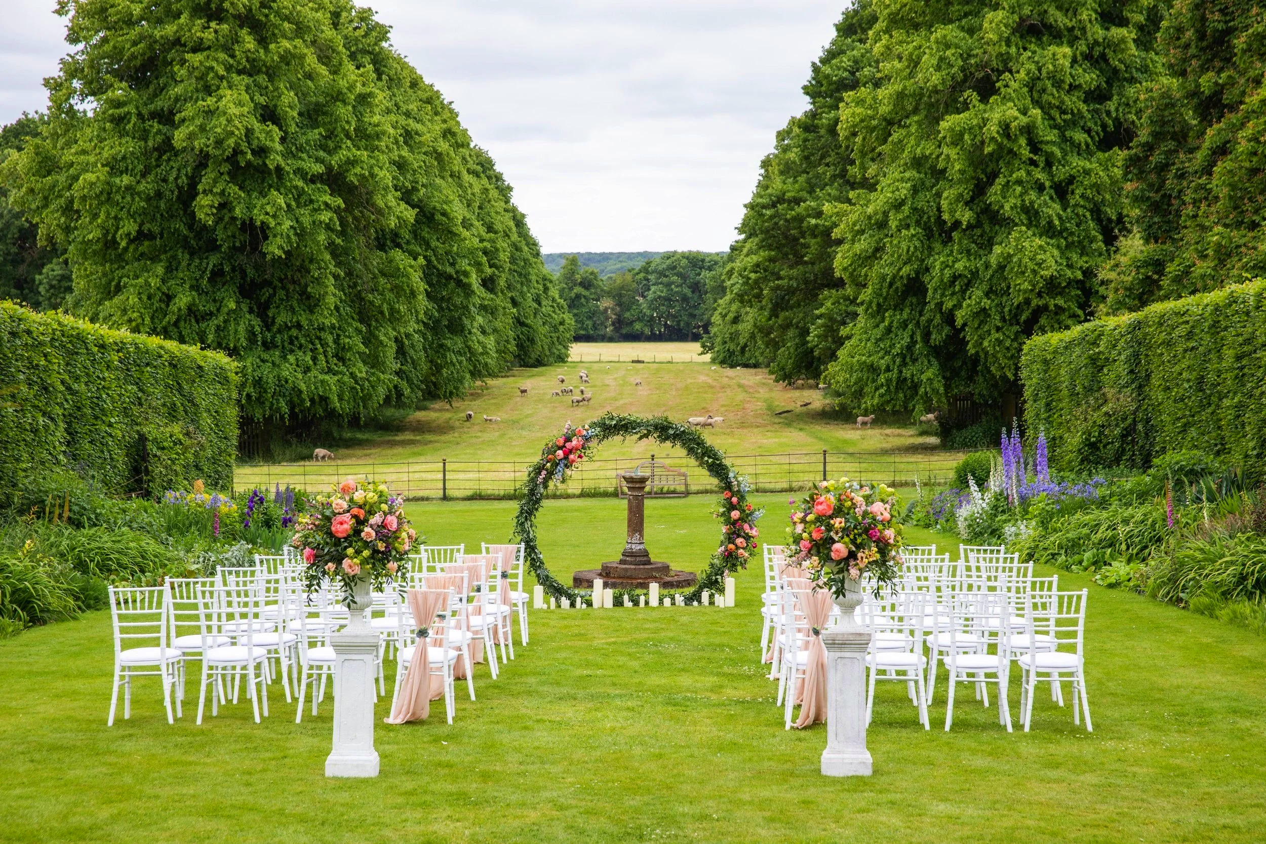 Outdoor wedding set up with white chairs and urns on plinths