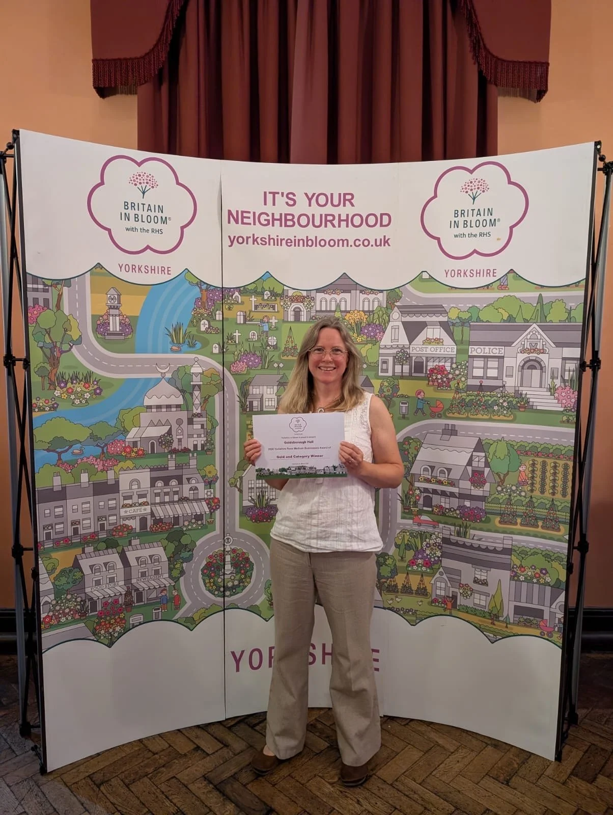 Image shows Goldsborough Hall's head gardener Debbie holding up a certificate with a gold award from Yorkshire in Bloom