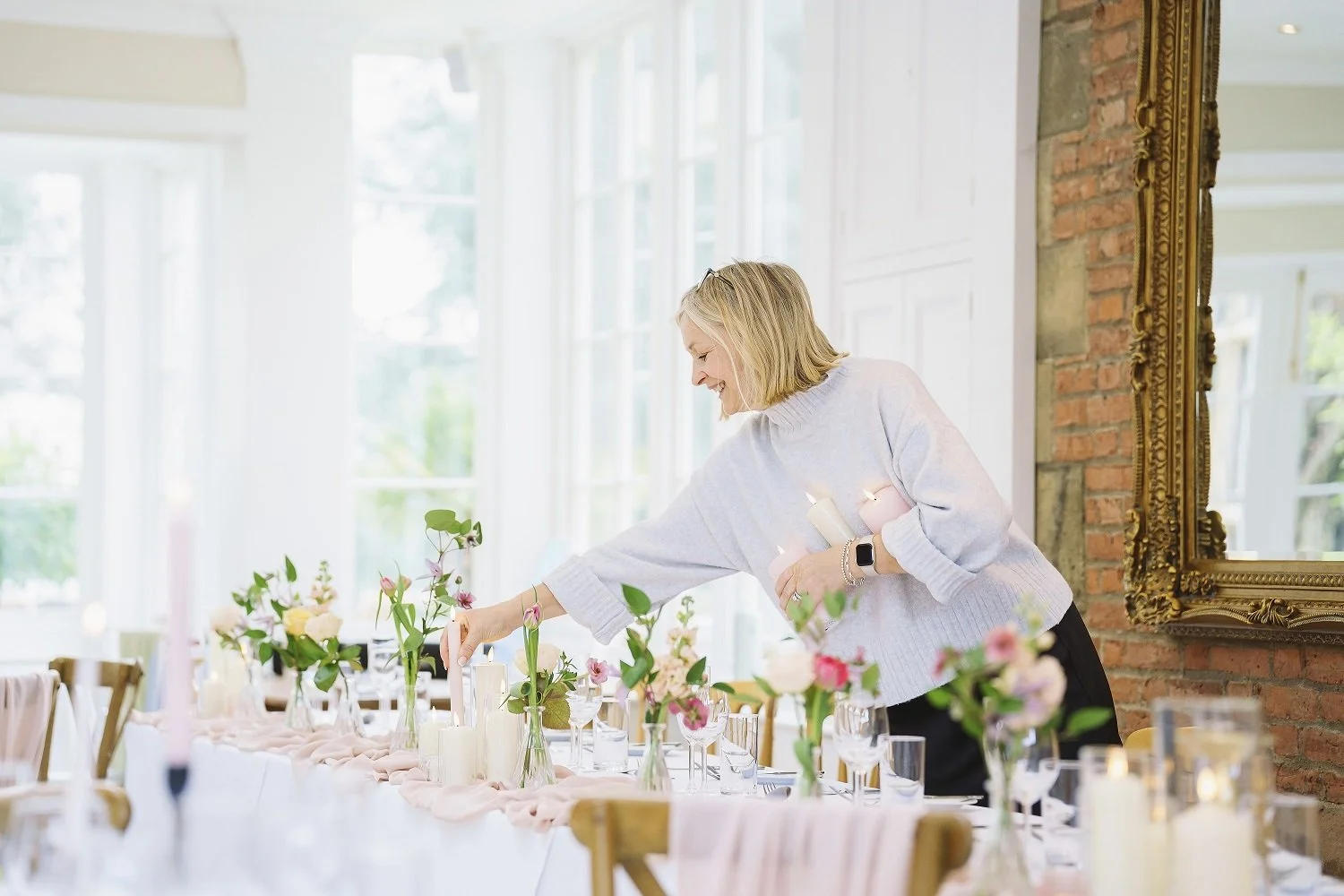 Shows an elegant lady reaching over a wedding breakfast table to adjust something in the Orangery at Goldsborough Hall, North Yorkshire