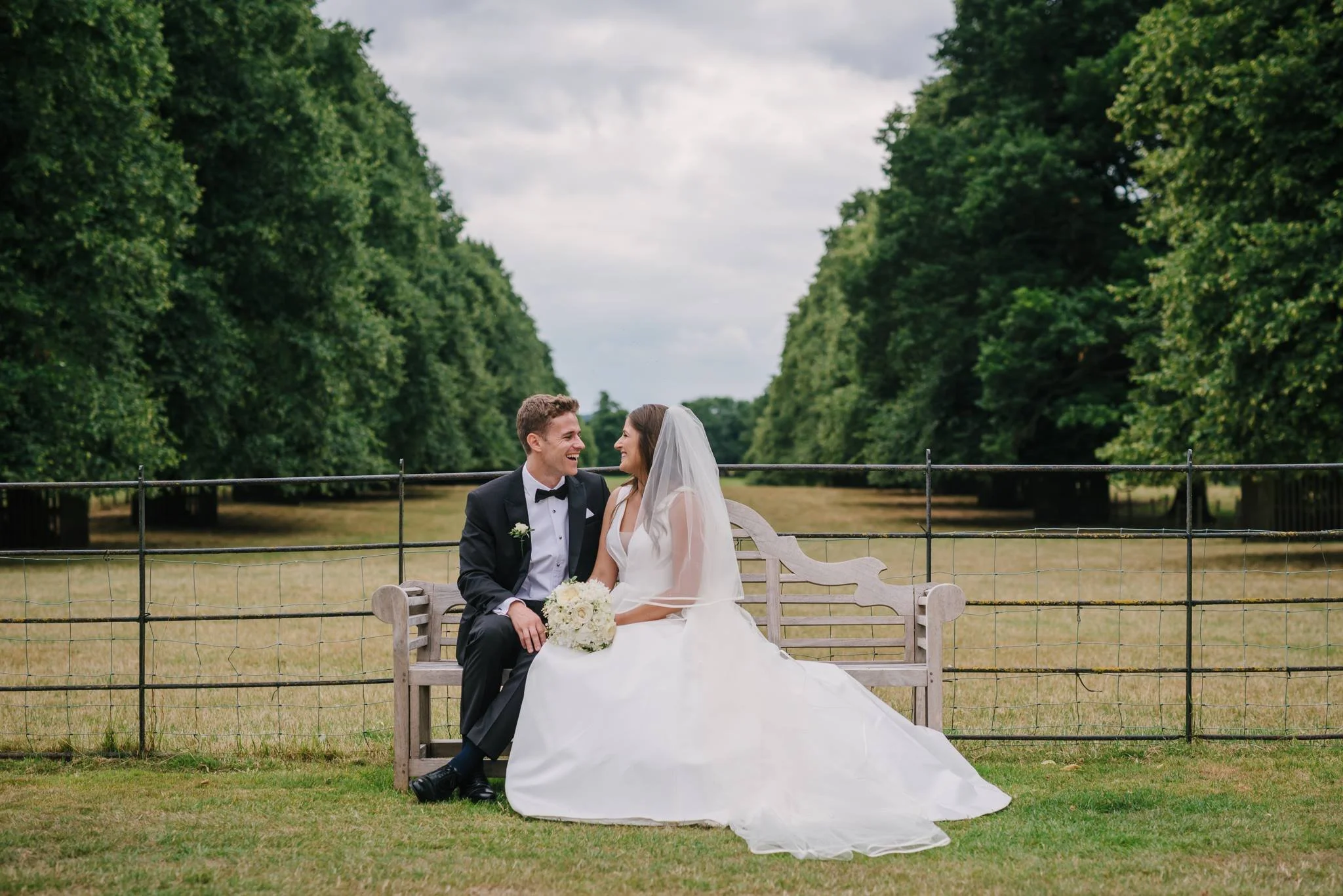 Wedding couple sitting on a bench with Goldsborough Hal's historic Lime Tree Avenue behind them