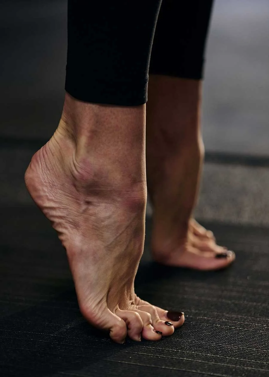 Close-up of a person's feet performing a yoga pose on a textured black mat, with black leggings visible.
