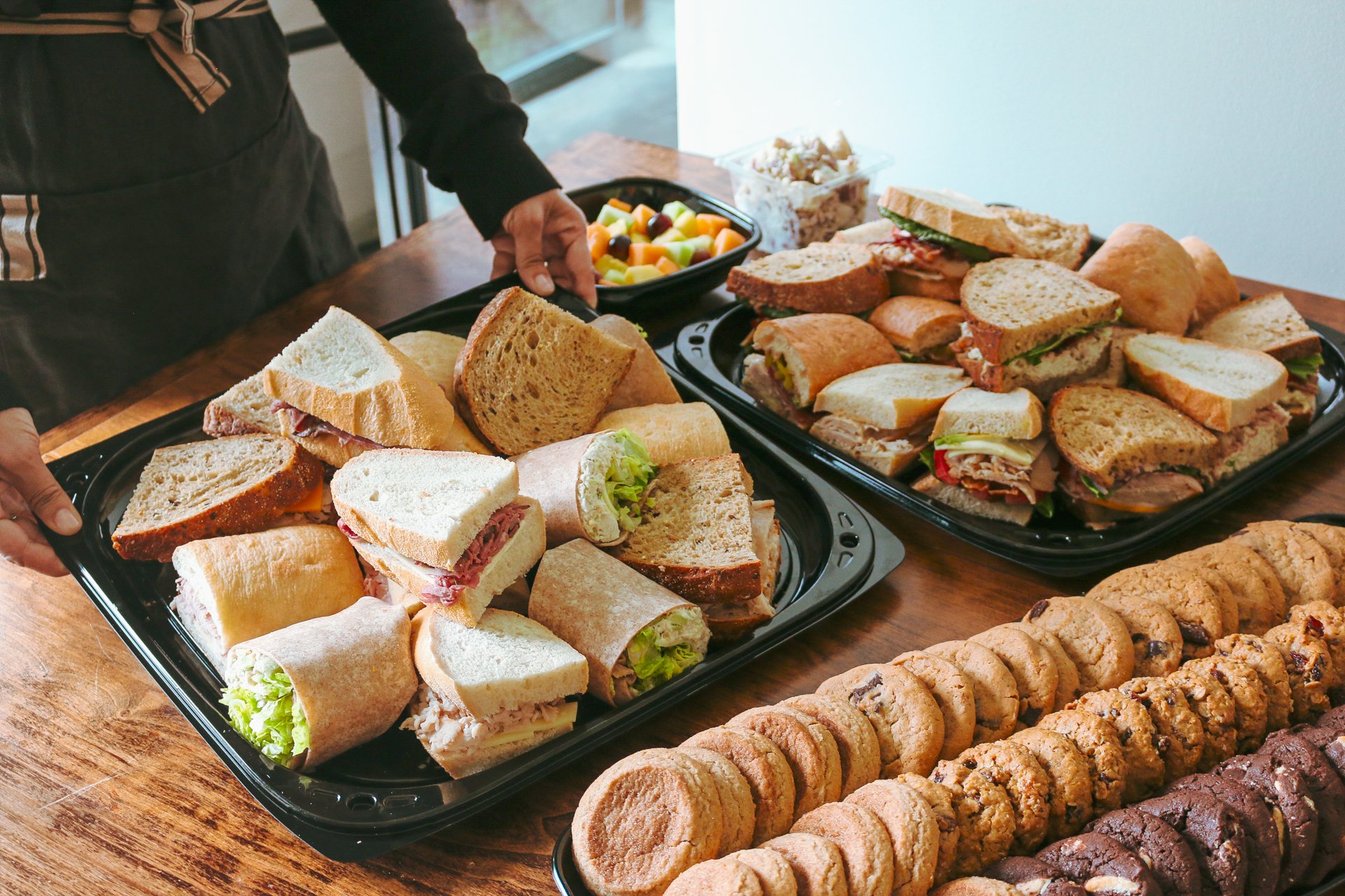 Two platters of sandwiches with cookies and fruit