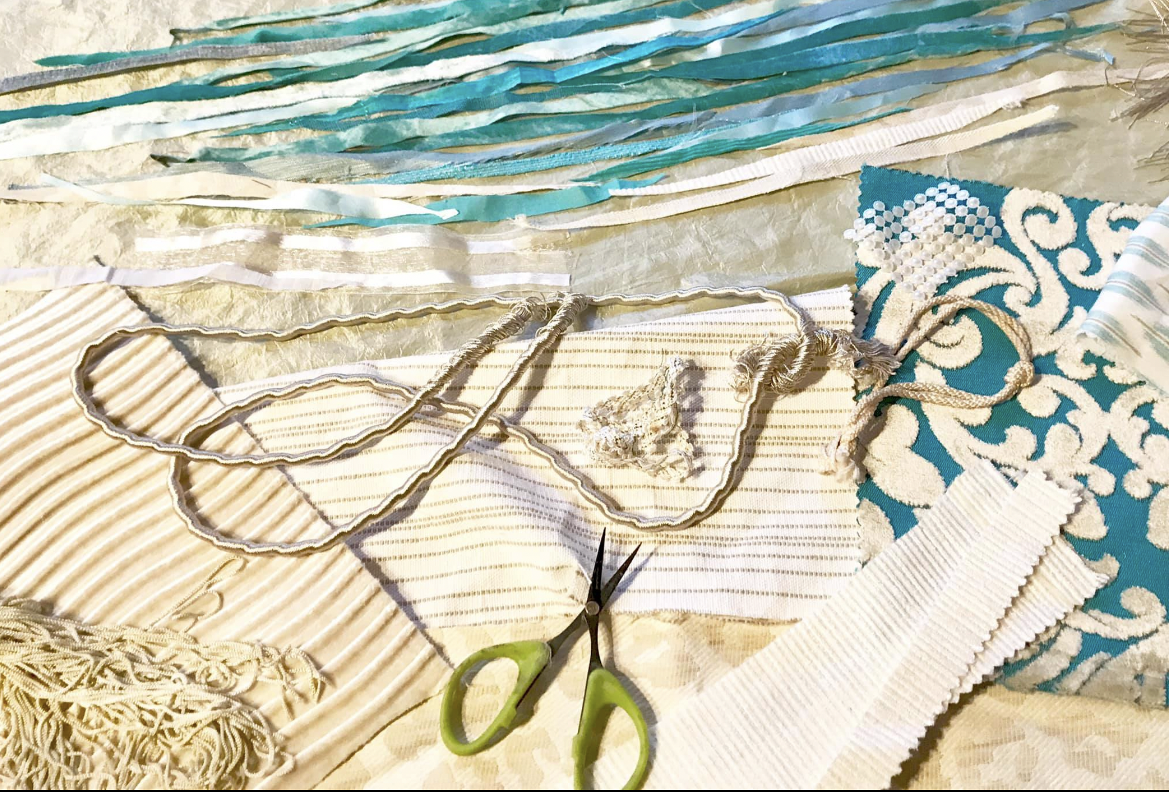 Various fabric swatches, ribbons, and lace on a table with a pair of green-handled scissors and a small piece of lace.