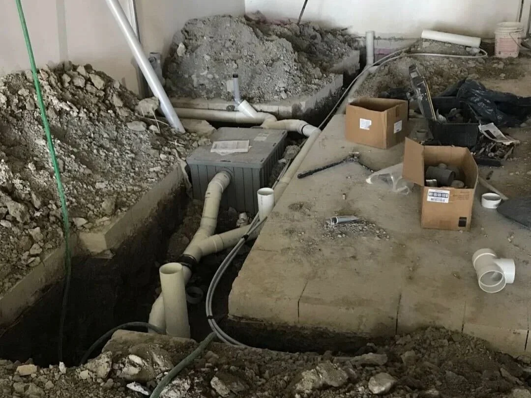 Construction site with exposed pipes, dirt, and construction tools and materials.