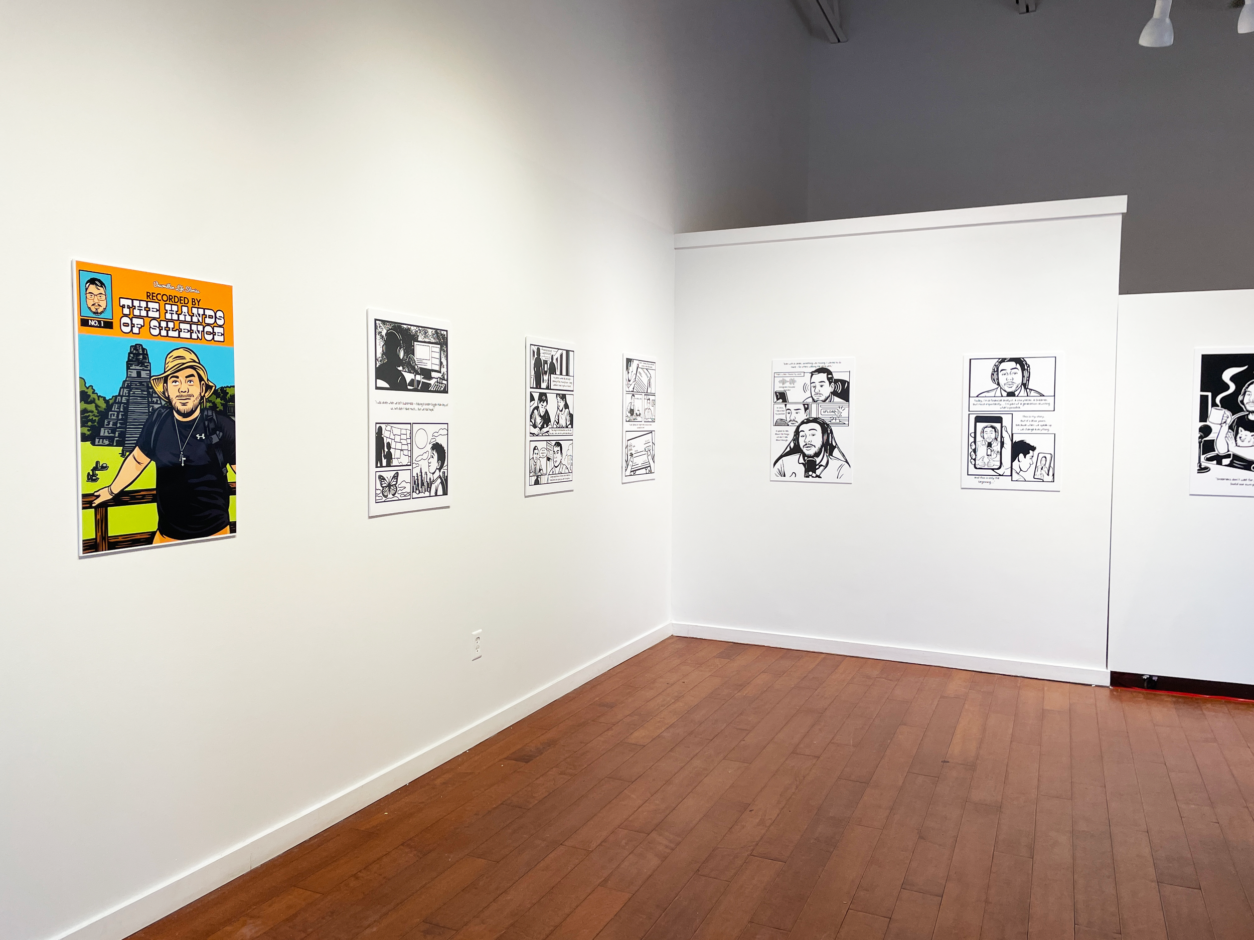 View of the inside of Fresh Eye Gallery. On a white wall, viewed at an angle, multiple, enlarged panels are displayed of the graphic novel, "Unwritten Life Stories, Recorded by the Hands of Silence," by artist Irving Vazquez.