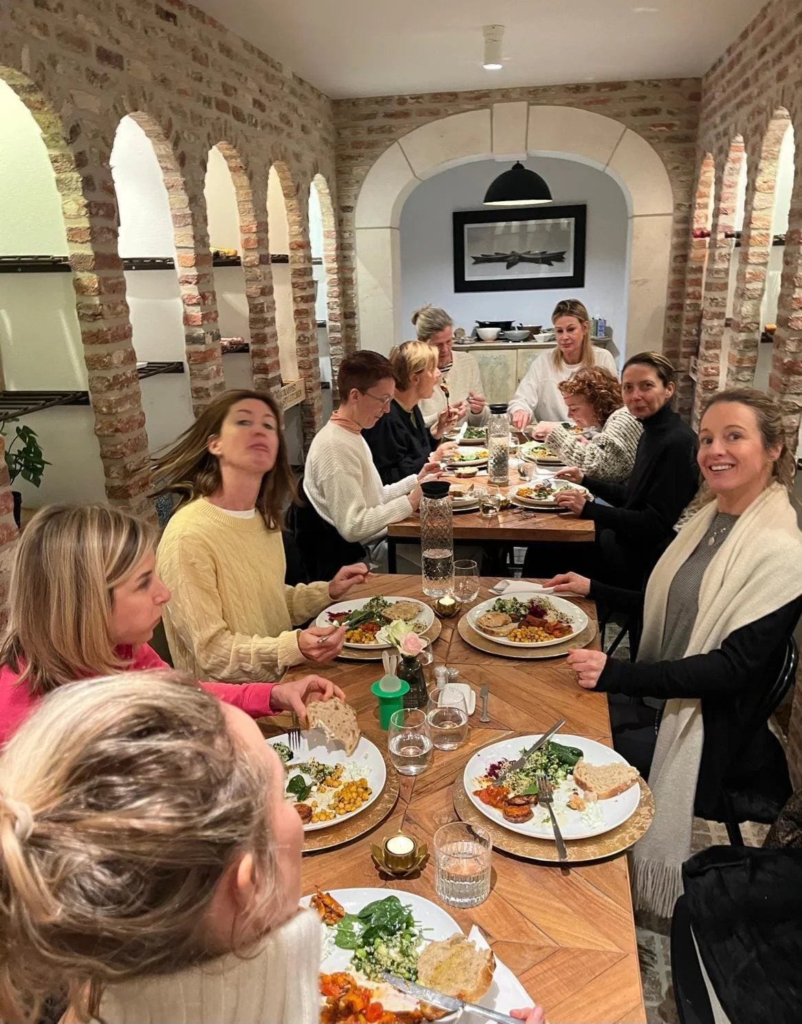 People gathered around a long dining table enjoying a meal in a rustic brick-walled room.