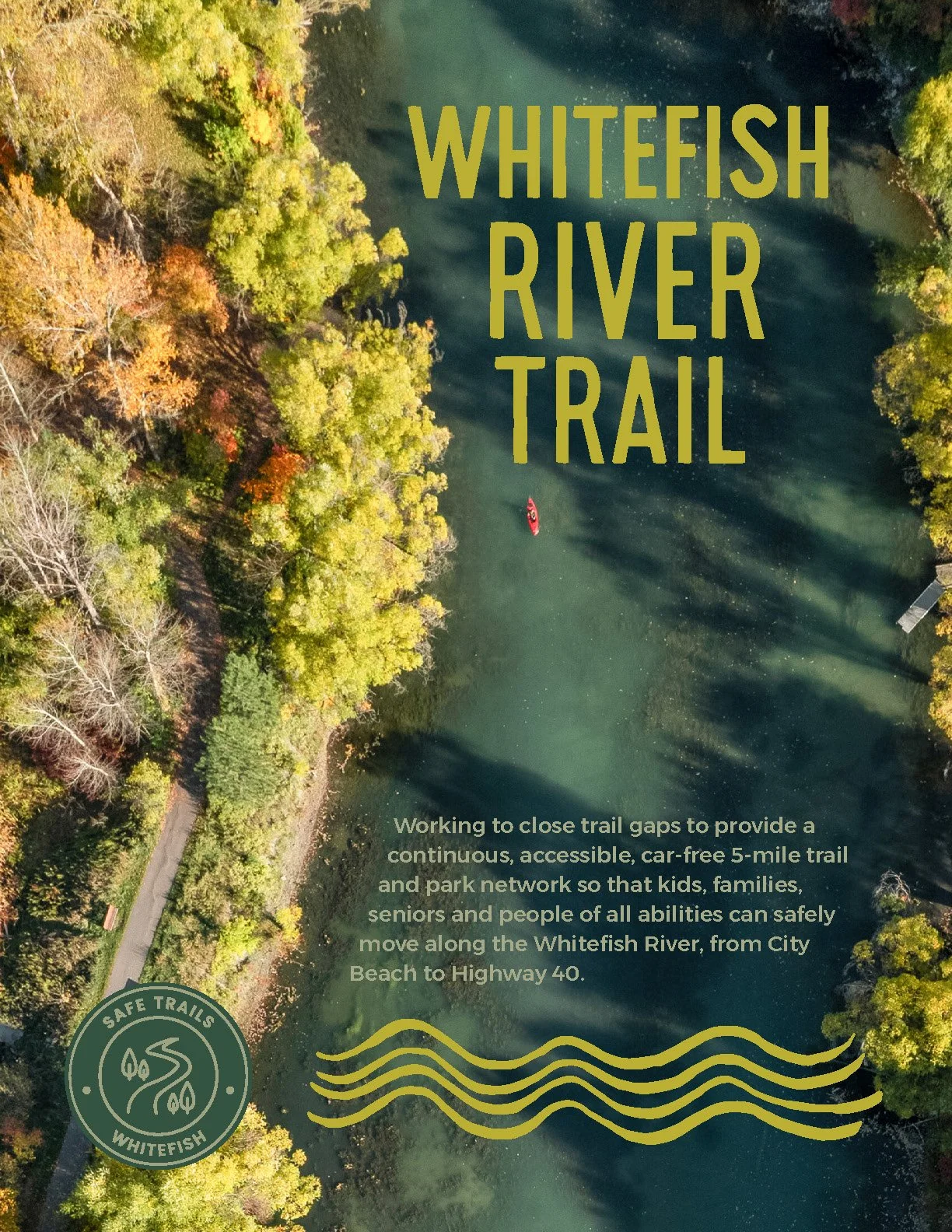 An aerial view of the Whitefish River with trees showing fall foliage along the riverbank, a person kayaking on the water, and part of a trail visible on the left side.