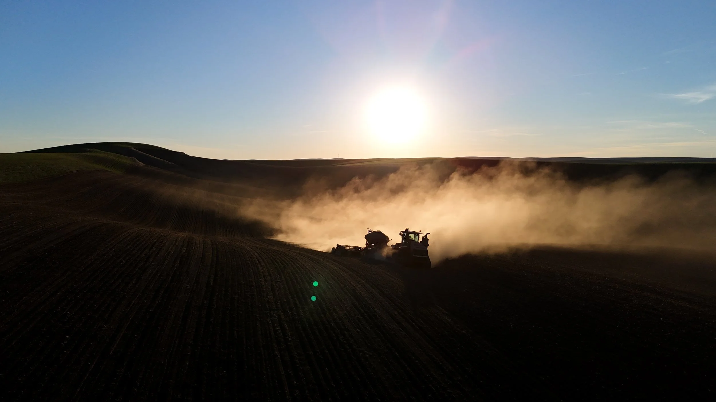 Tractor pulling disc drill on the Palouse hills in the sunset, with dust floating behind.