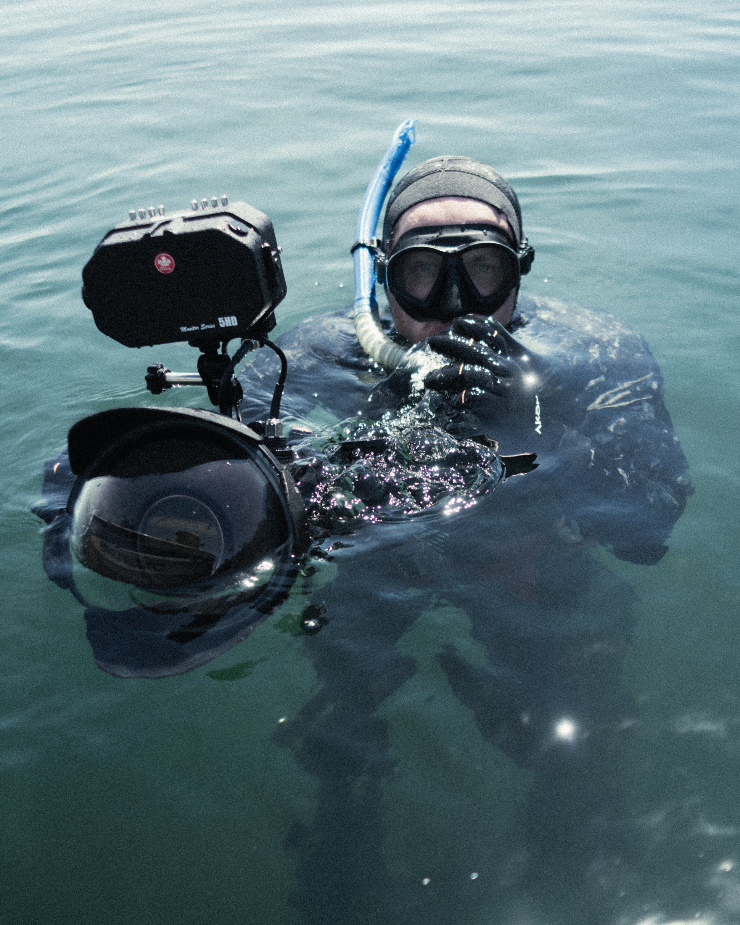 A person in snorkeling gear, including a black mask and snorkel, swimming in water with a mobile camera mounted on a stabilizing device.
