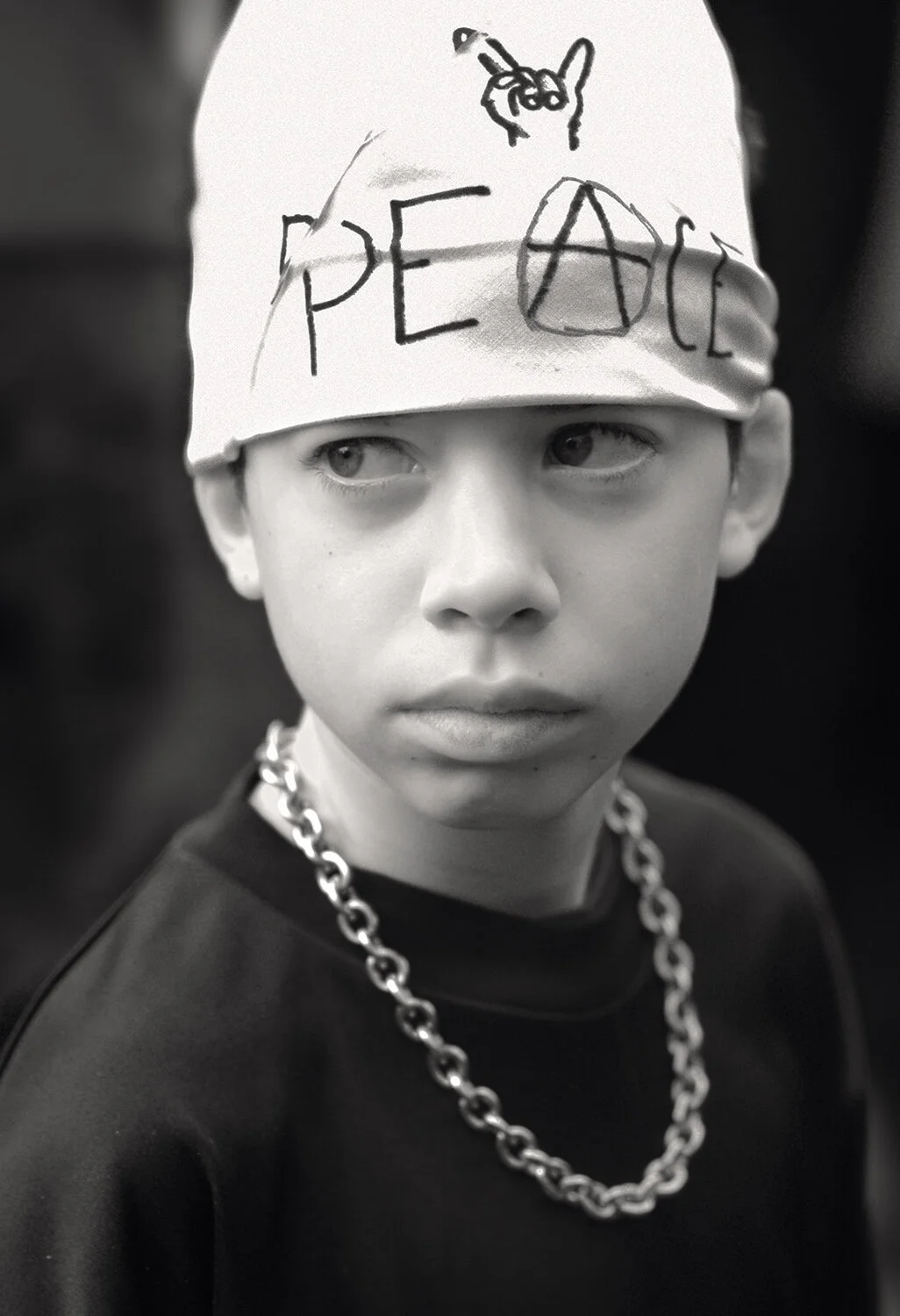 A young  demonstrator, dressed completely in black except for his decorated cap, strikes a militant pose in contrast to the more muted mood of the Women in Black. His wandering gaze expresses ambivalence toward a future threatened by adults; an incip
