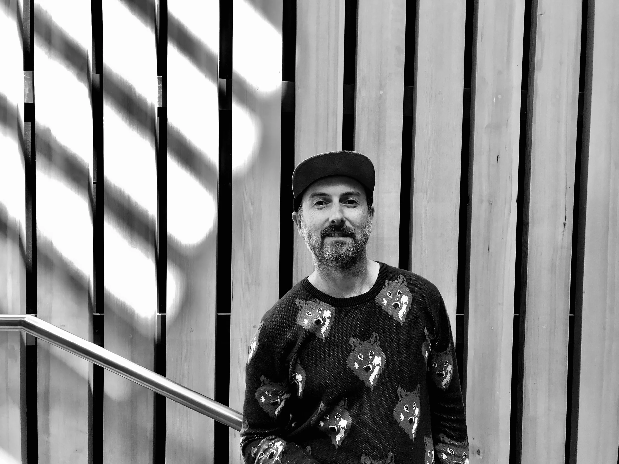 Aidan Ward, founder of Yellow Tail Wood Studio, in front of a slatted wood wall.