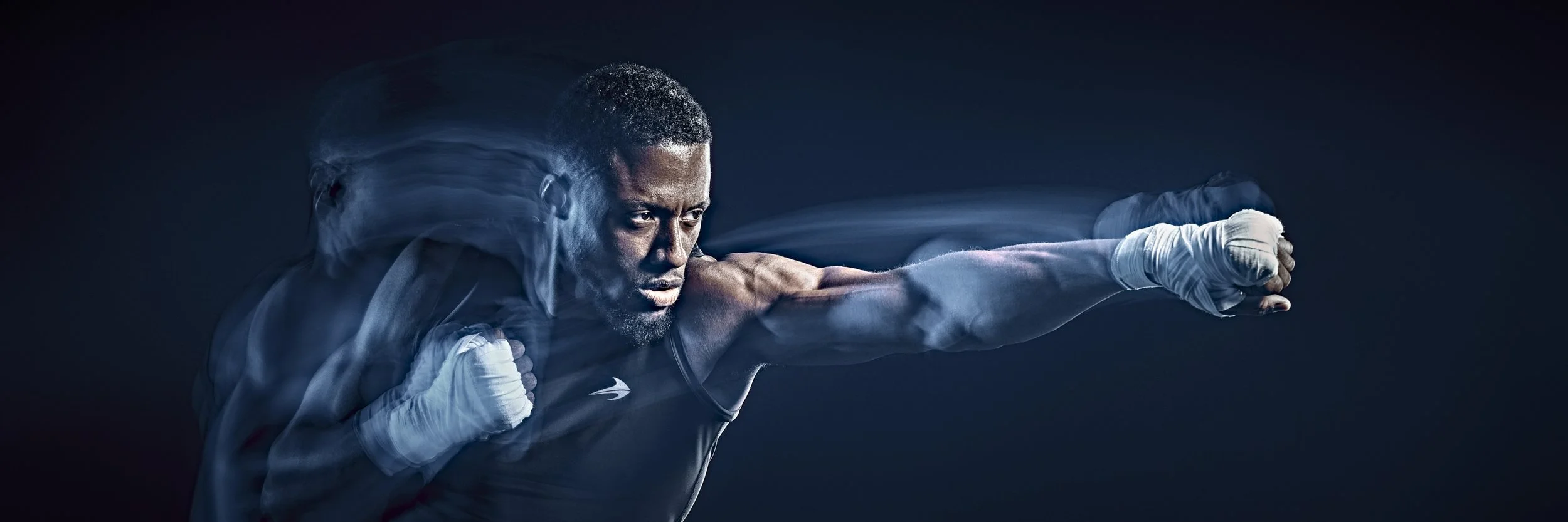 A male boxer in a fighting stance throwing a punch, with motion blur and a dark background.