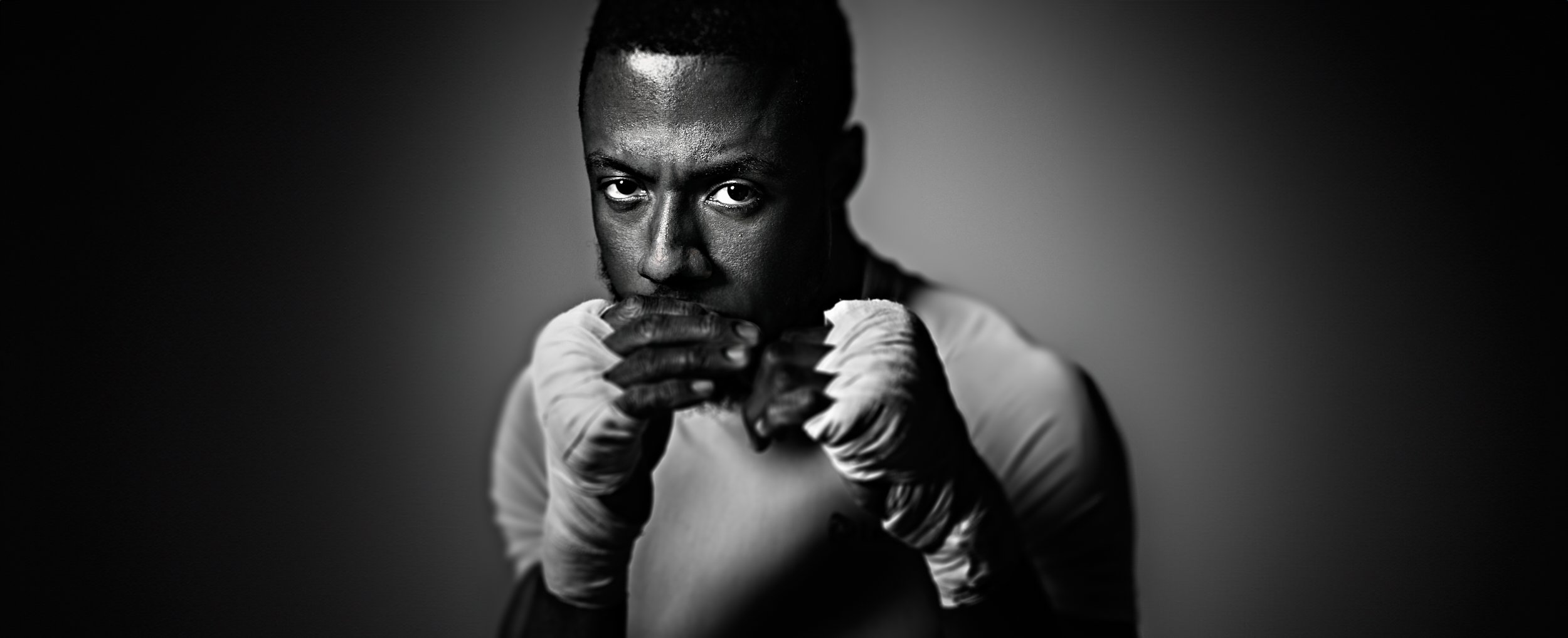 Black and white portrait of a male boxer with a serious expression, wearing boxing gloves, facing forward with fists raised.