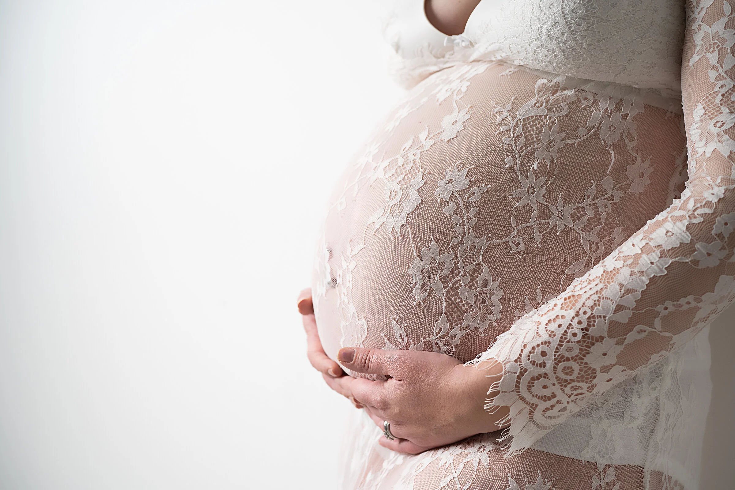 Pregnant woman holding her belly, wearing a white lace dress with floral patterns.