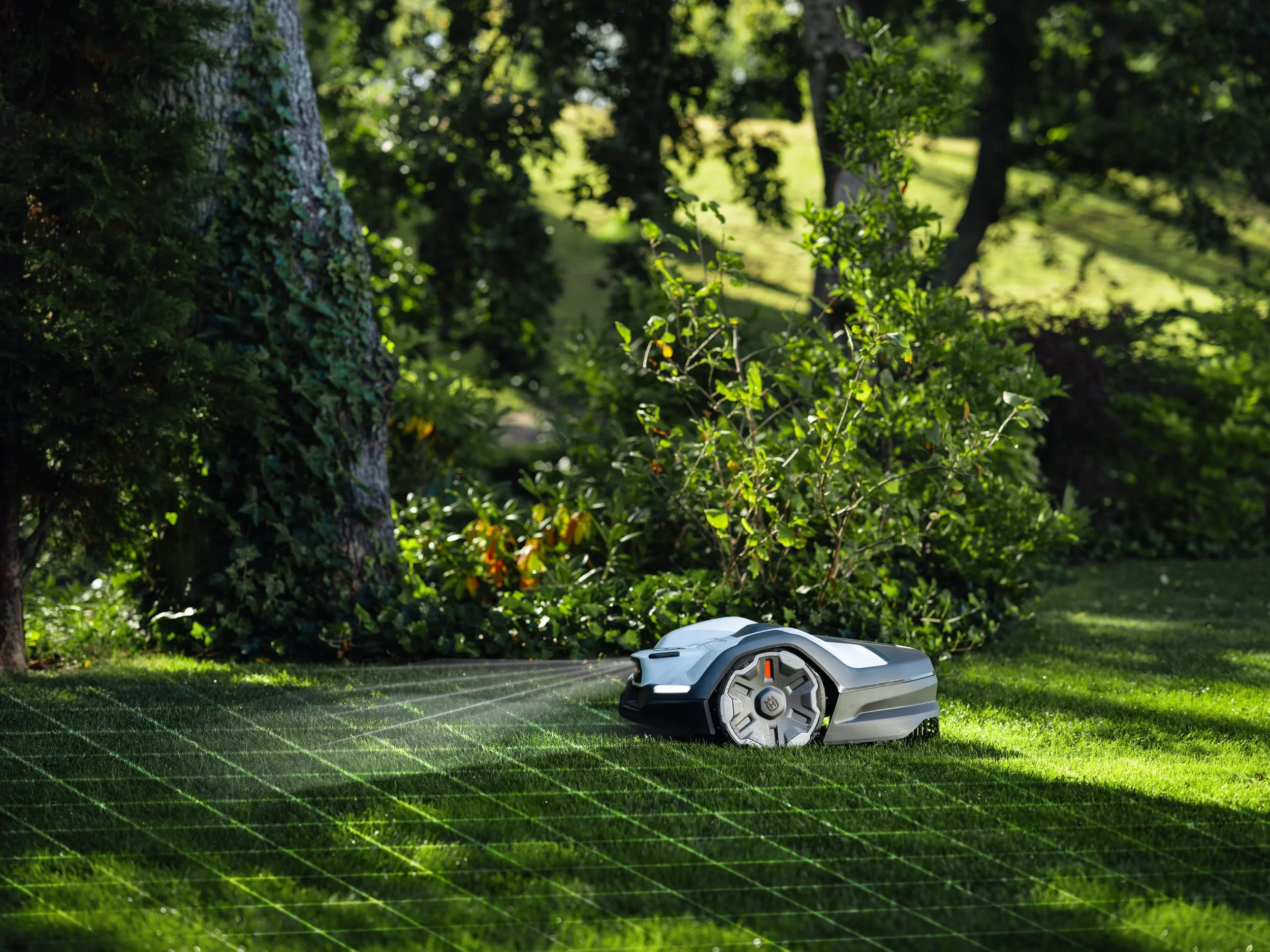 A robotic lawn mower cutting grass in a lush, green outdoor garden with trees and bushes.