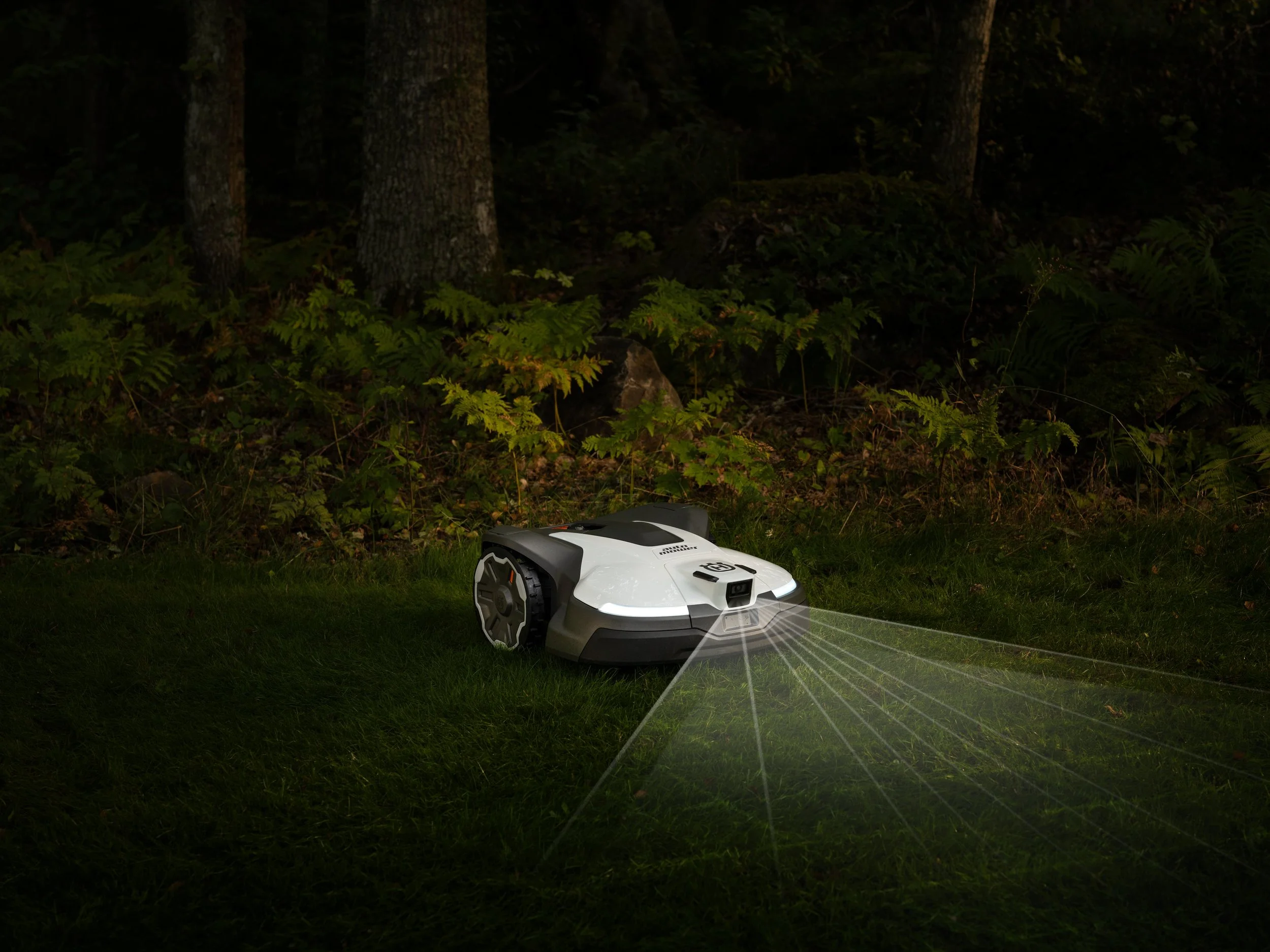 A robotic lawn mower cutting grass in a wooded yard at night.