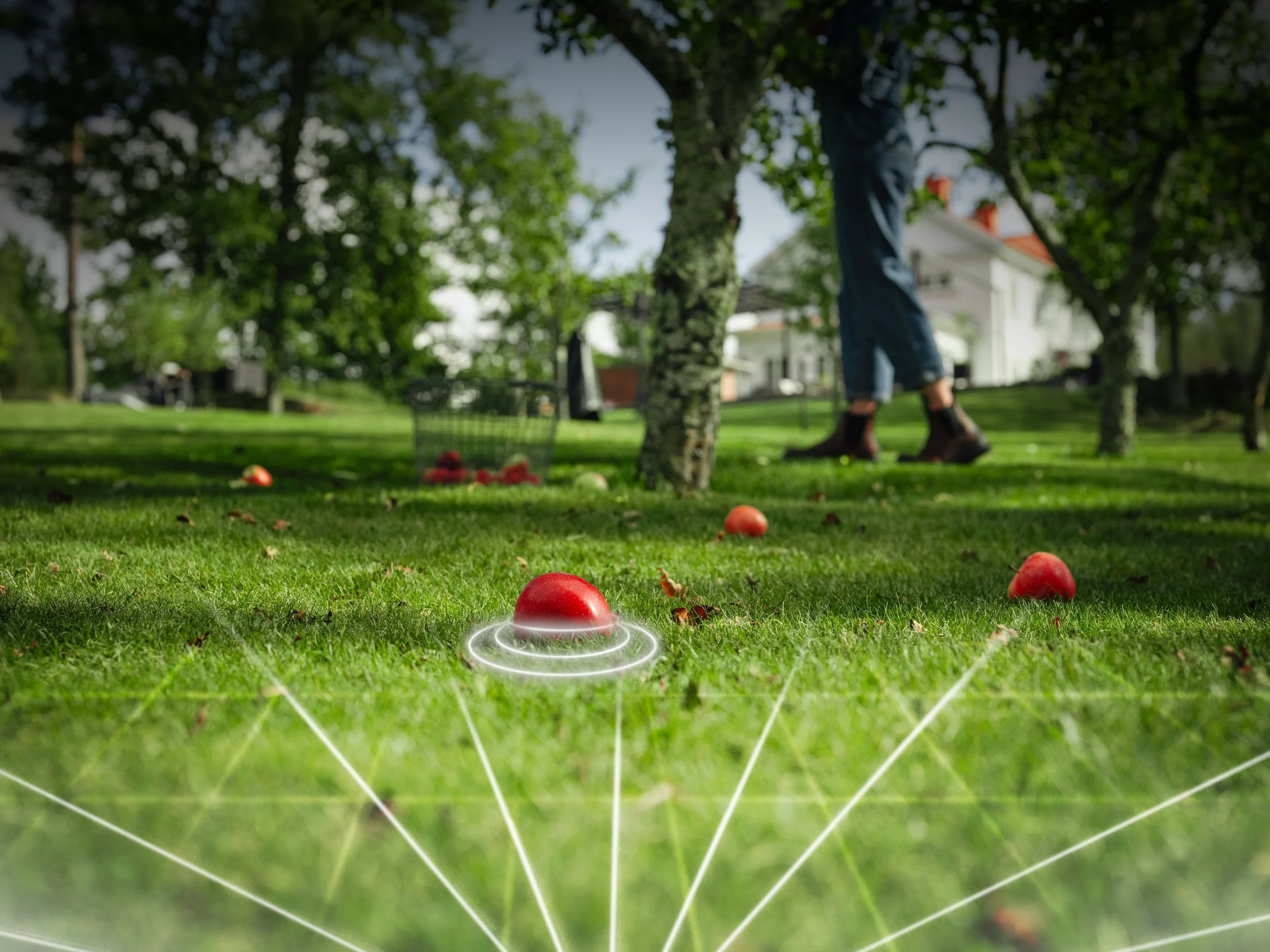 A golf ball is on the ground with a digital overlay of lines and a red ball above it, in a lush green yard with trees and a house in the background.