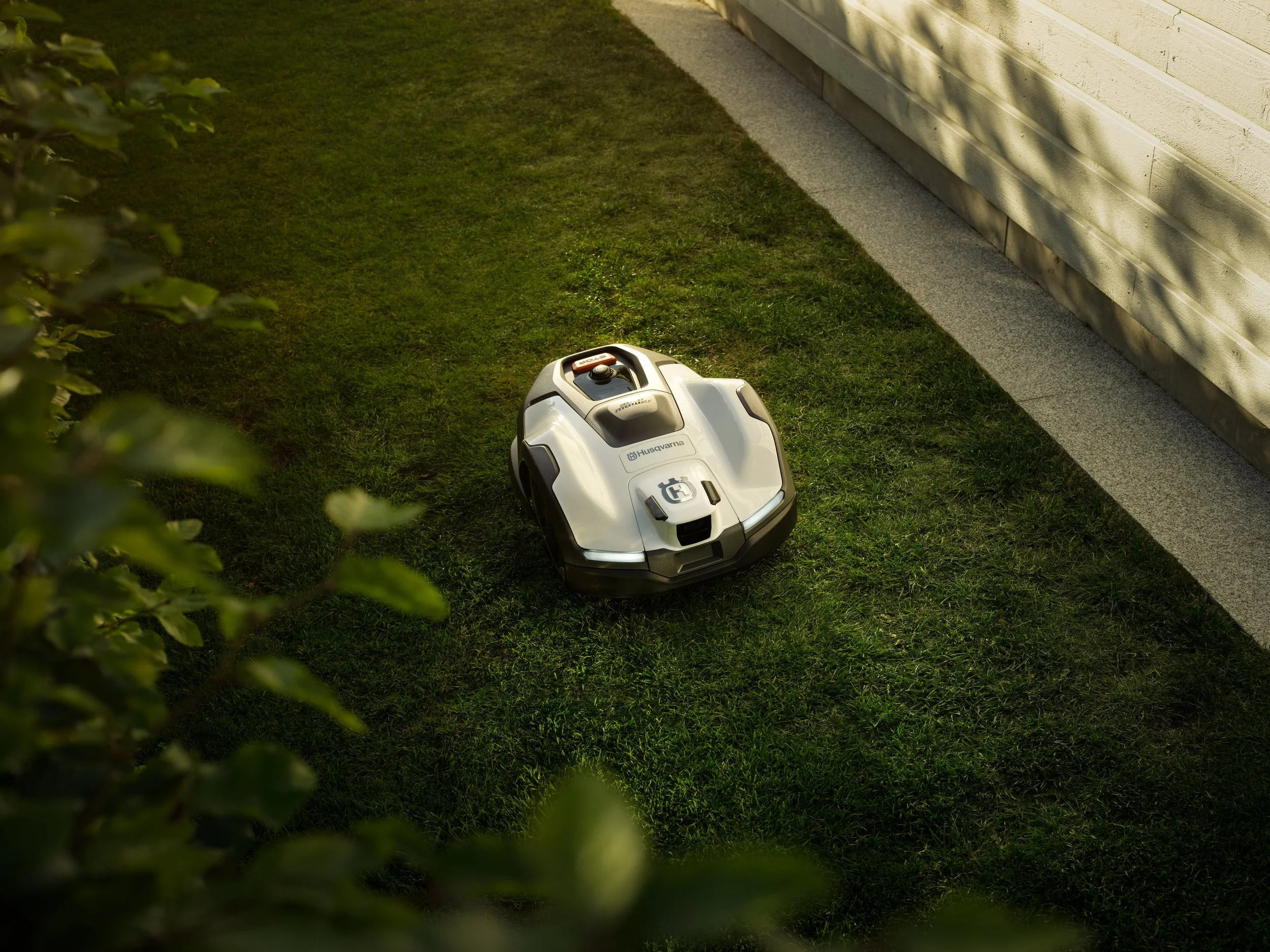 A robotic lawn mower on green grass near a light-colored house with a gray walkway.