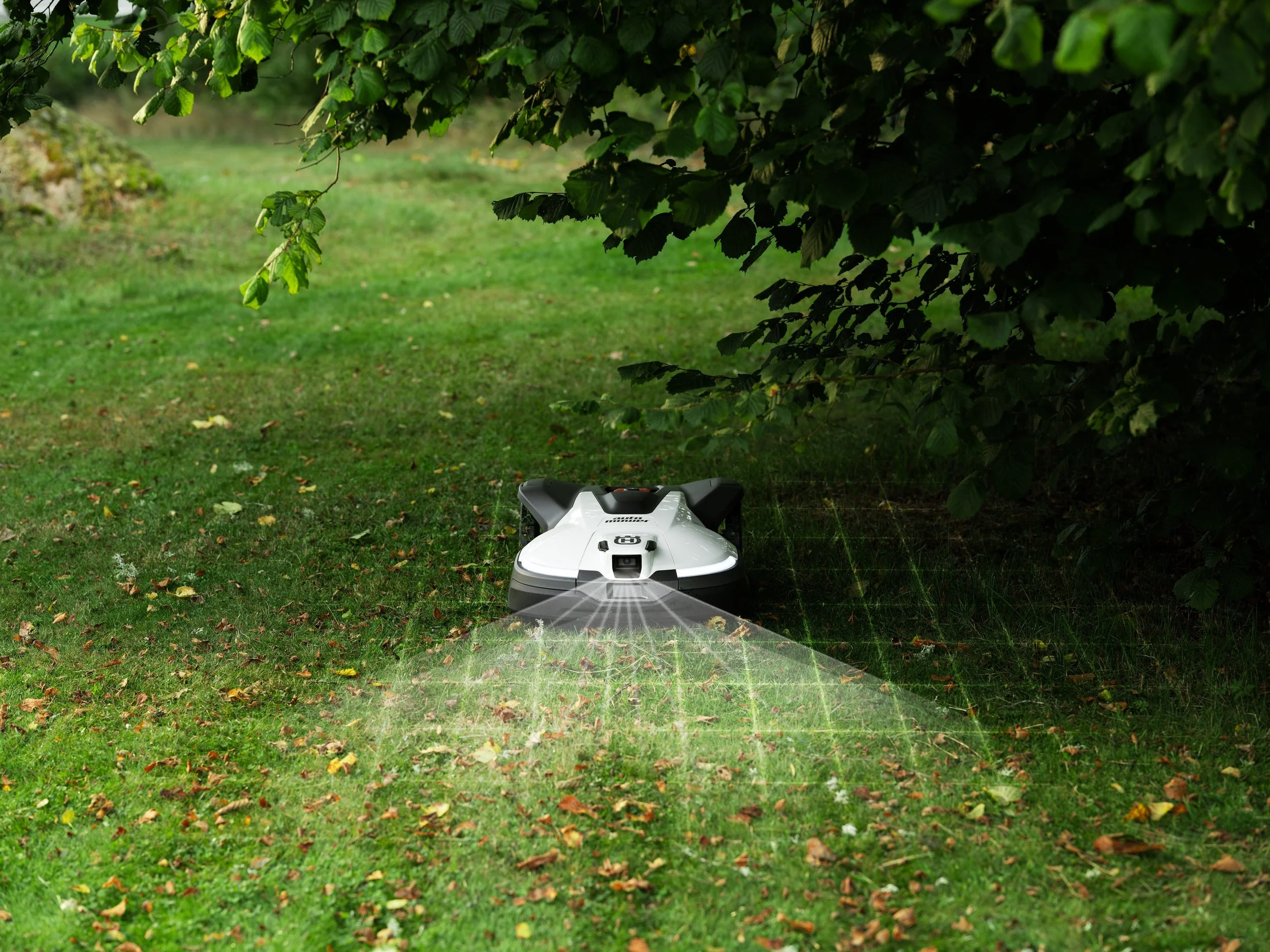 Robot lawn mower trimming grass in a green outdoor garden under a tree