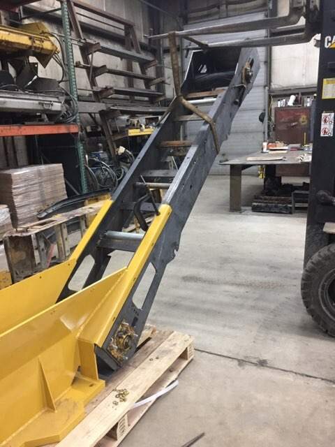 Industrial forklift attachment with a yellow metal scoop, likely used for lifting or transporting materials, inside a workshop.