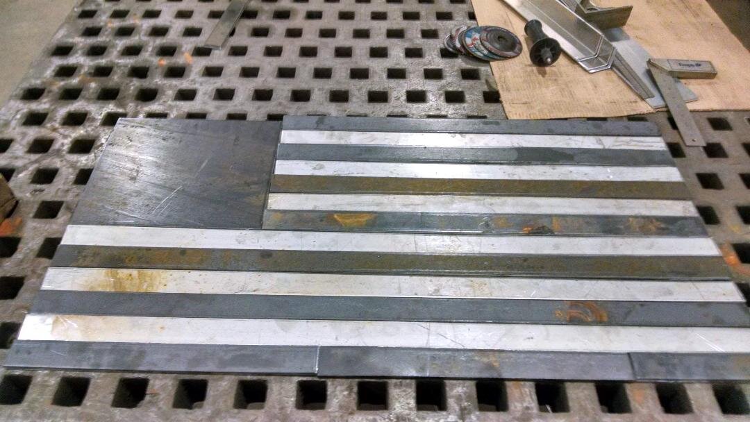 Metal sheet flag resembling the American flag with black and white stripes on a workbench.