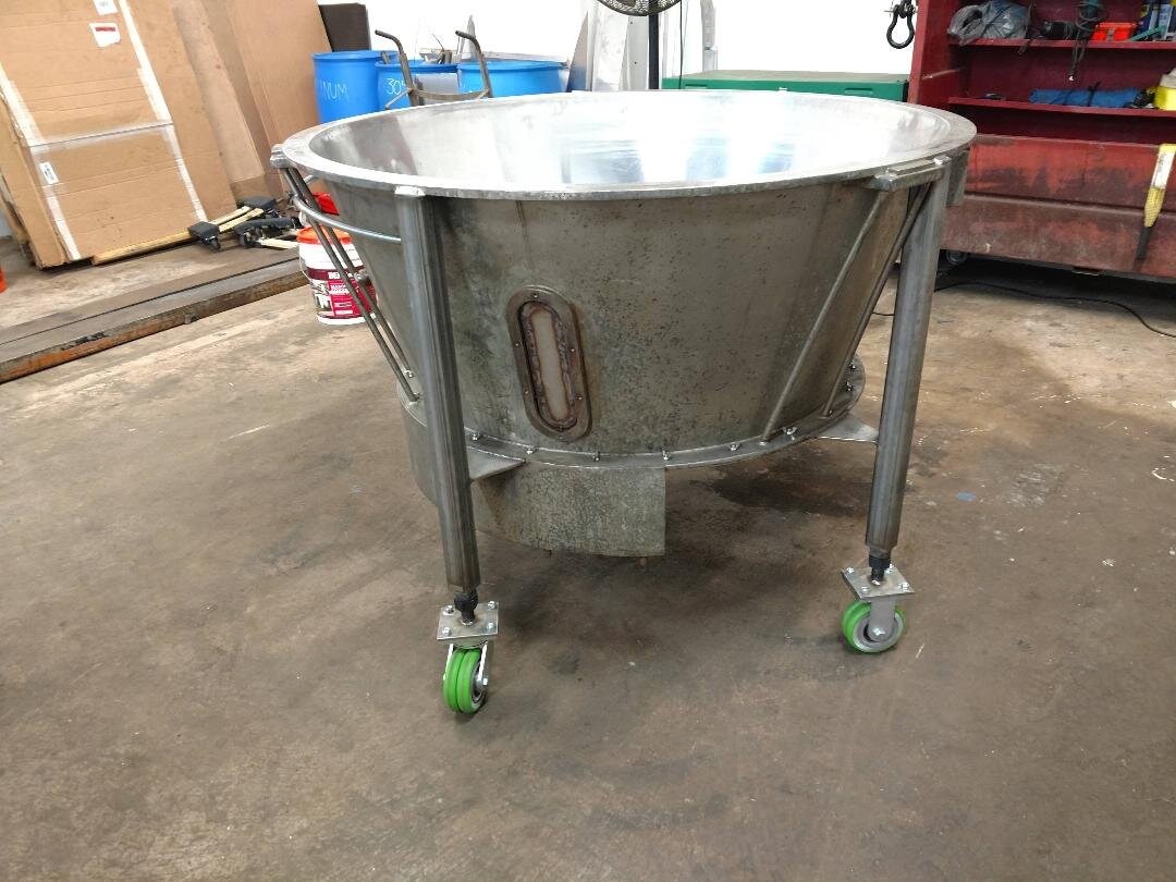Large industrial metal funnel with wheels in a workshop environment, surrounded by various tools and equipment.